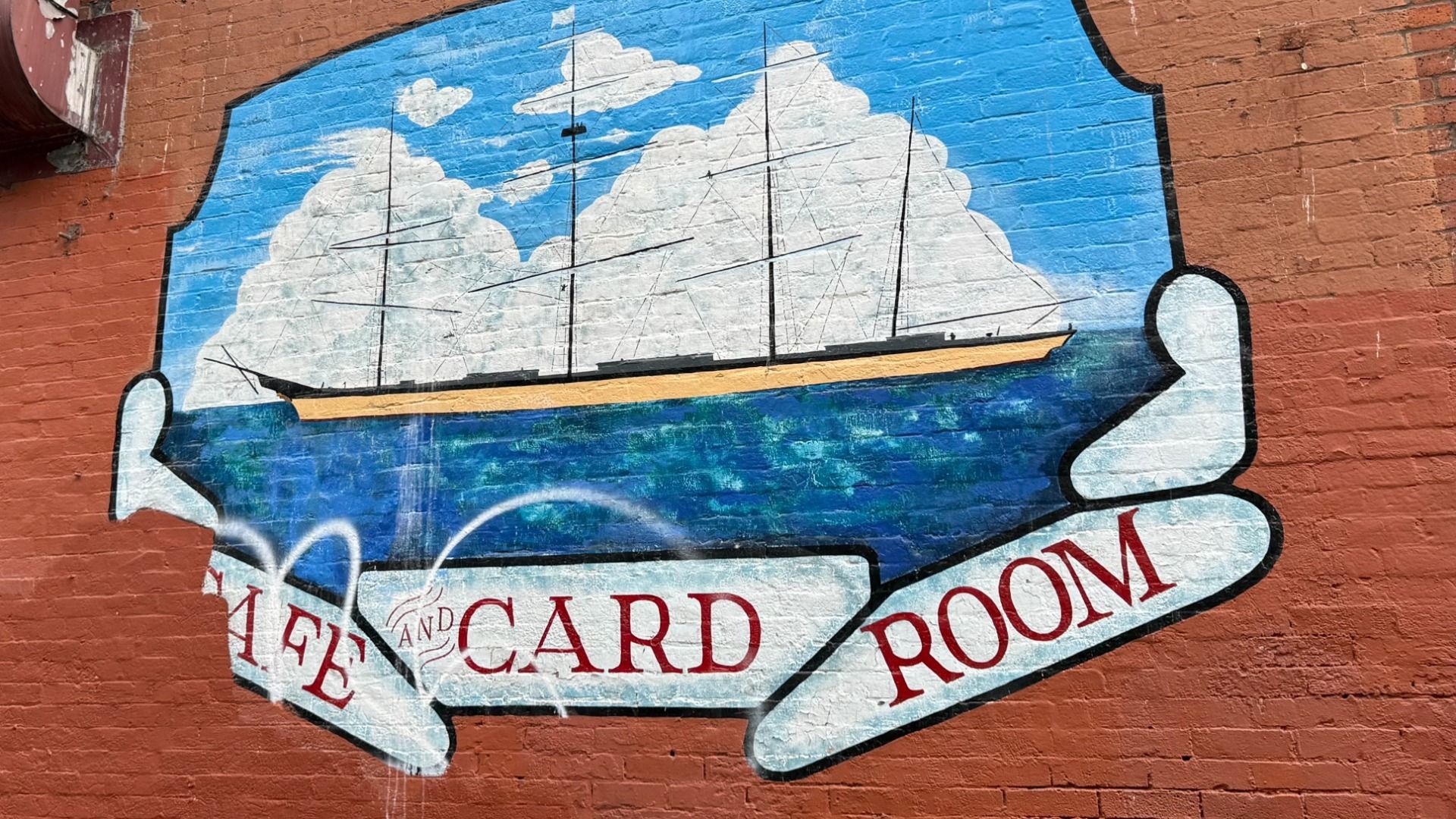 Mountains and sailboats are painted on a brick wall with the words "Cafe and Card Room".