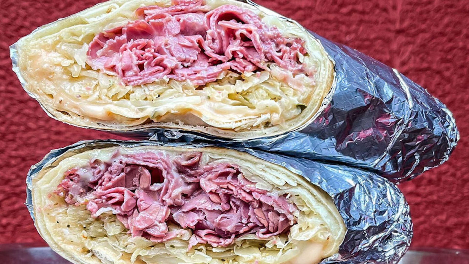 Two halves of a Reuben wrap in foil stacked atop each other. 