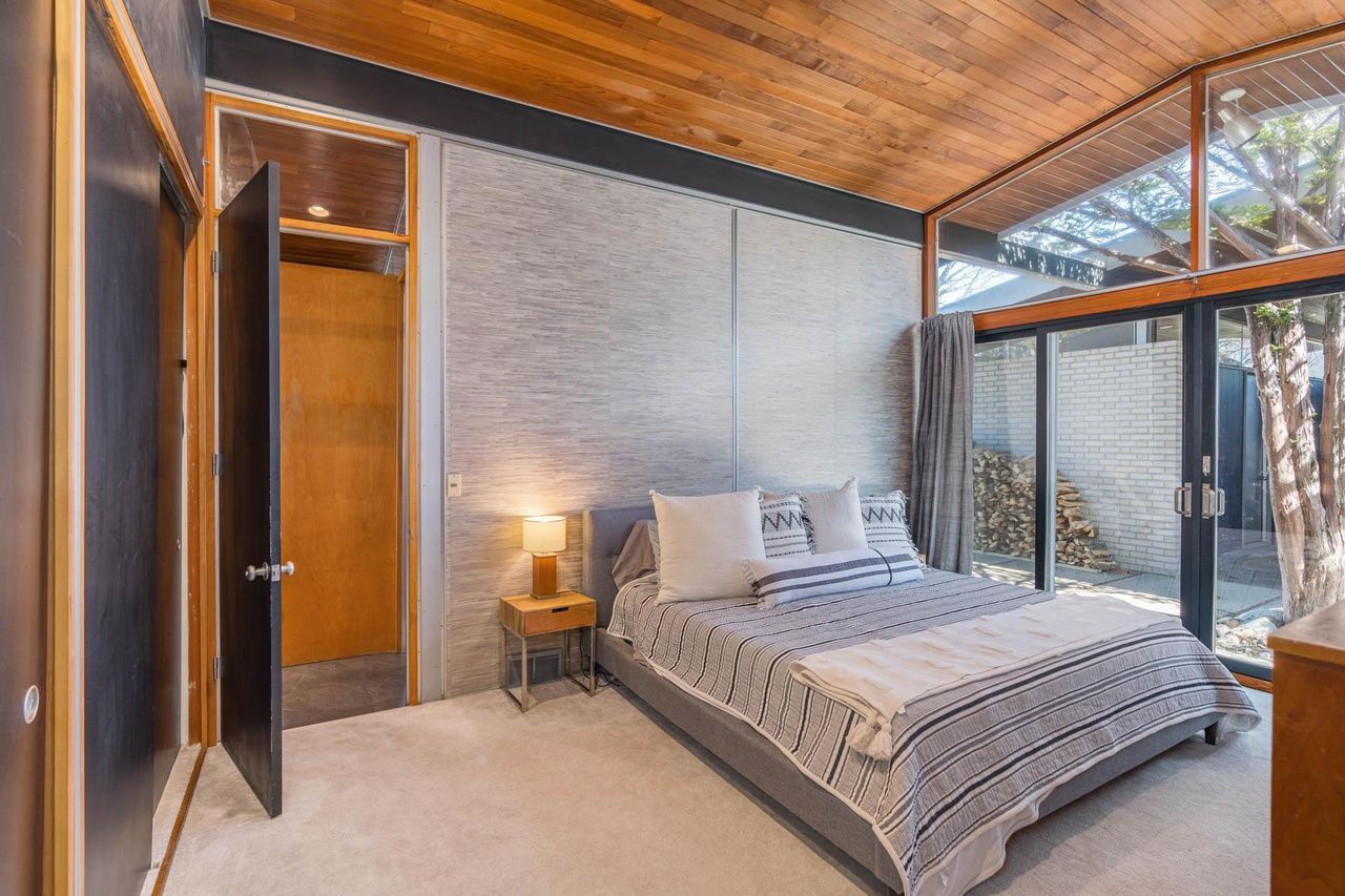A mid-century modern style bedroom with glass walls and a bed with gray furniture.
