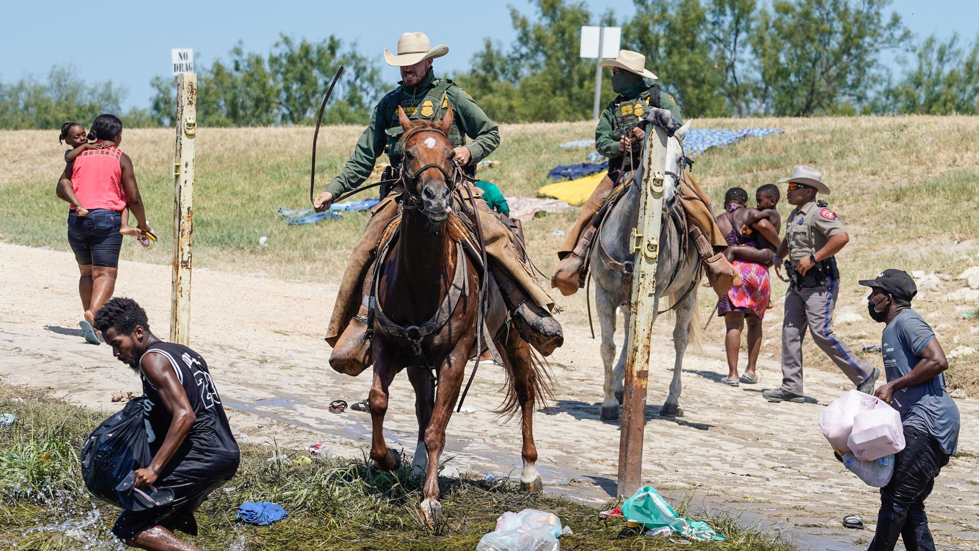 Photo of a U.S. Border Patrol agent sitting on horseback holding a long rein in a whipping motion as they face off against a migrant who's running back into the water