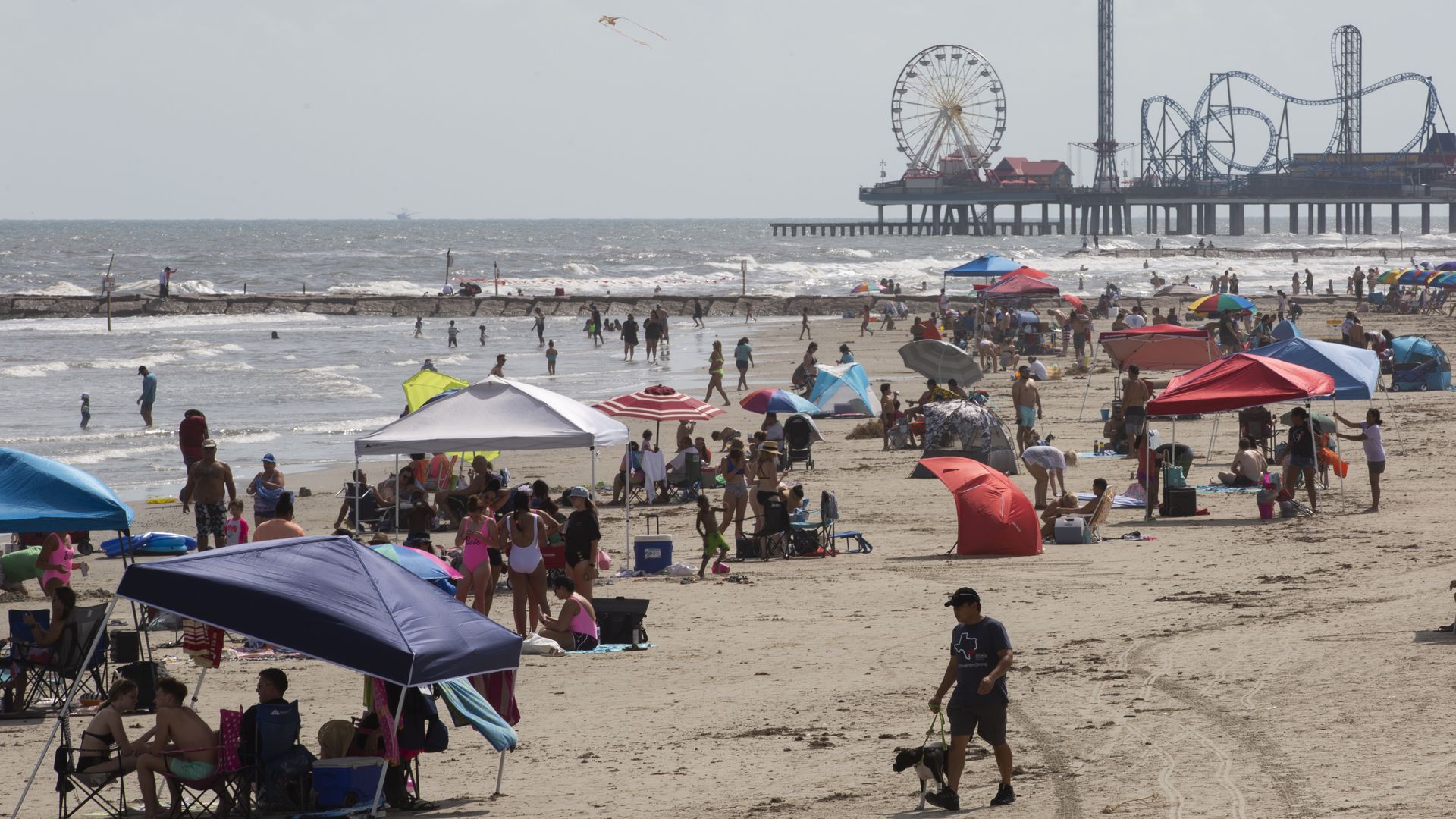 Wide shot of beachgoers in Galveston with Pleasure Pier in the background 