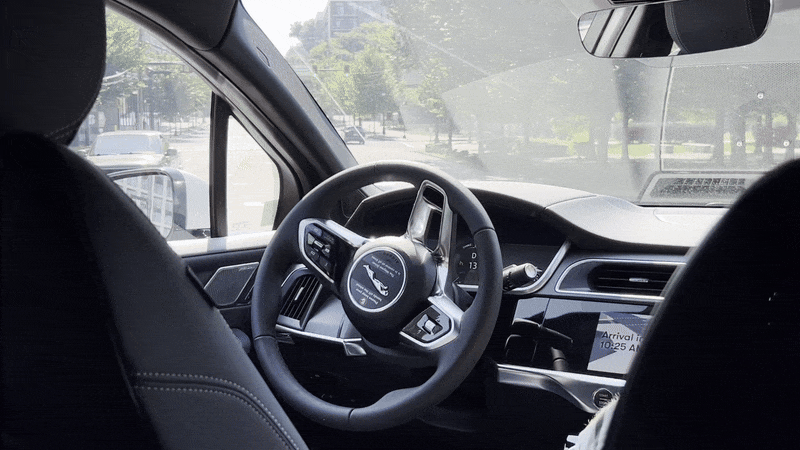 A GIF of a driverless taxi operating in traffic while a person sits in the seat next to them