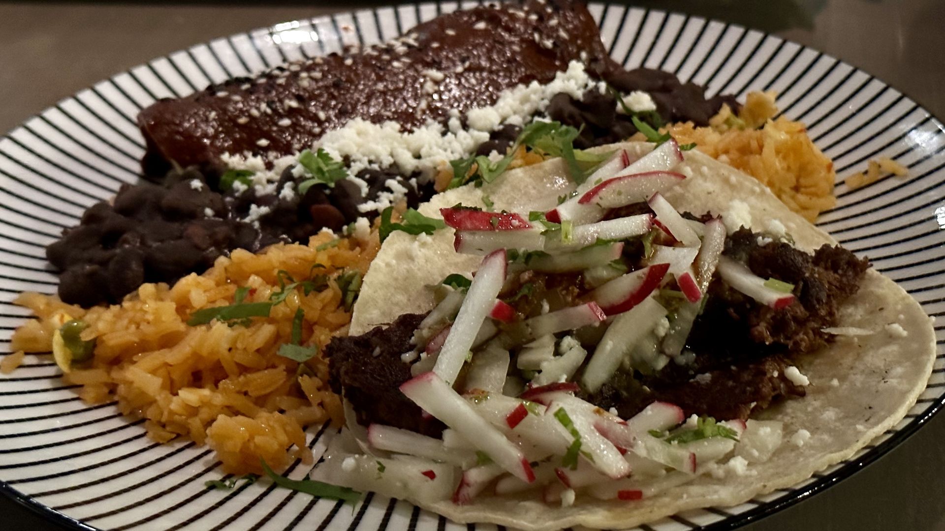 A taco with rice and beans on a black and white plate
