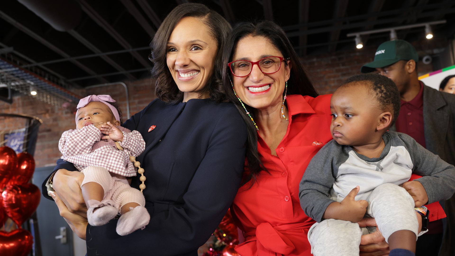 Two women hold babies and smile for a posed photo.