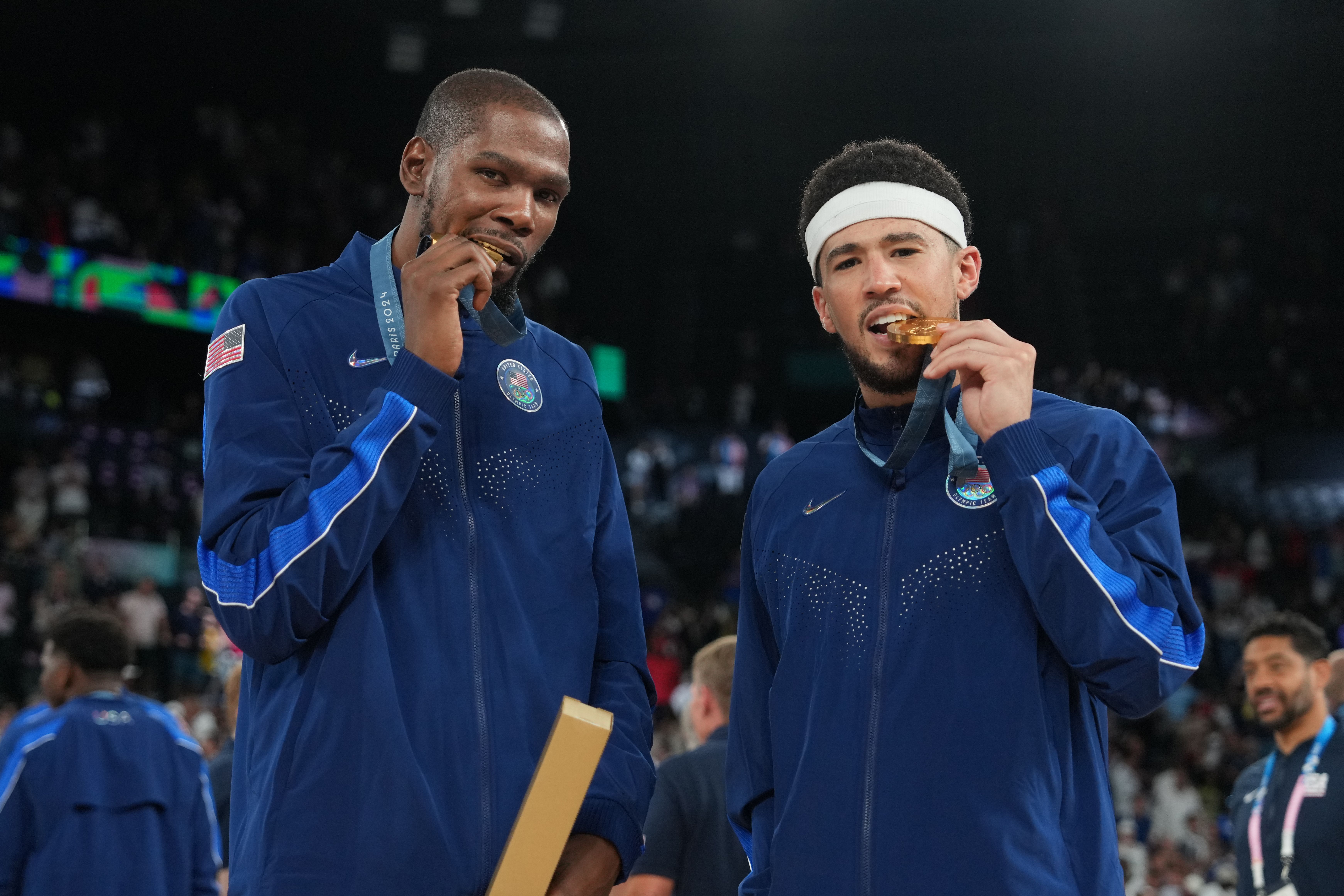 Two basketball players biting on their gold medals. 