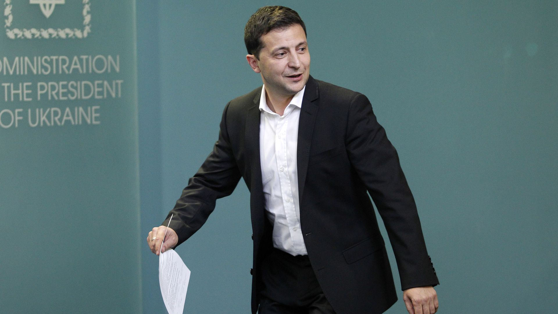 In this image, Zelensky walks while holding a piece of paper.