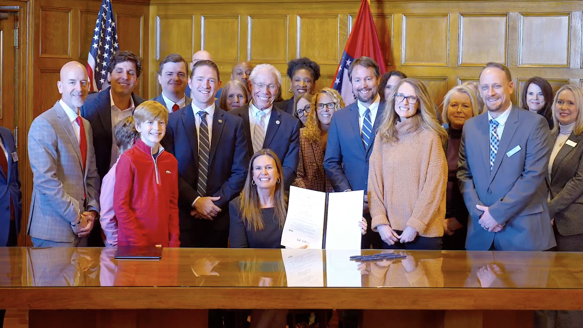 A screenshot of Arkansas Gov. Sarah Huckabee Sanders signing a bill into law, flanked by lawmakers an children.