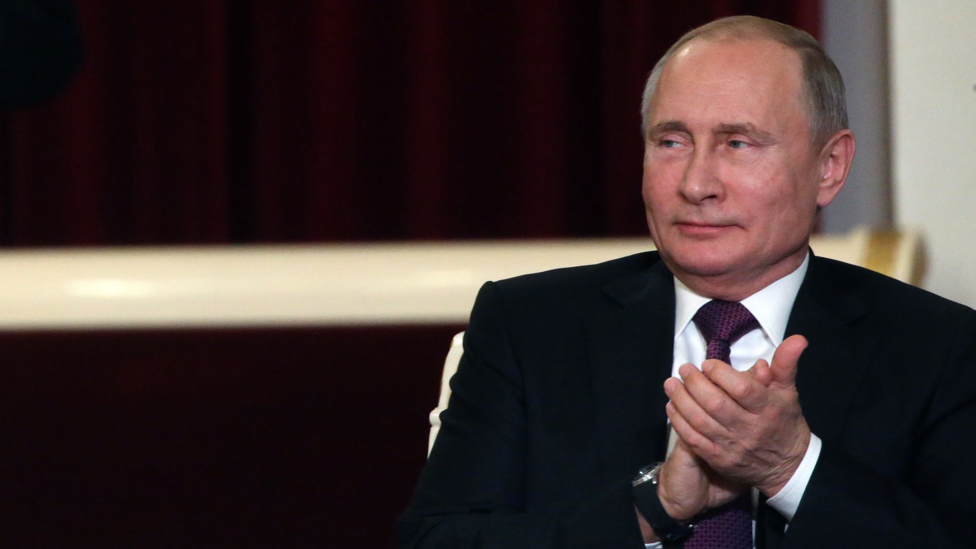Vladimir Putin glances to his right while clapping his hands together