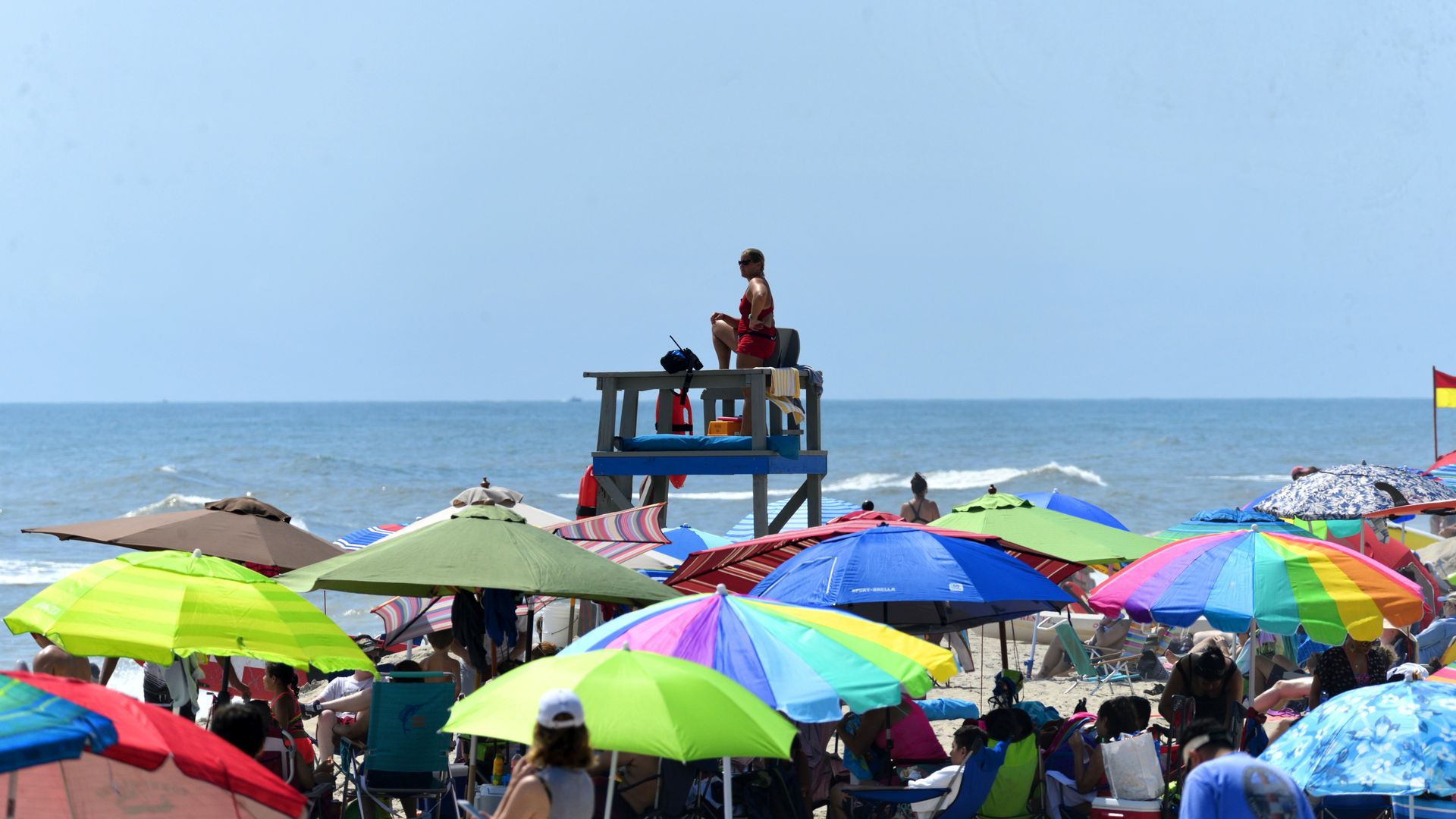 A lifeguard on a stand surrounded by colorful beach umbrellas and beach goers.