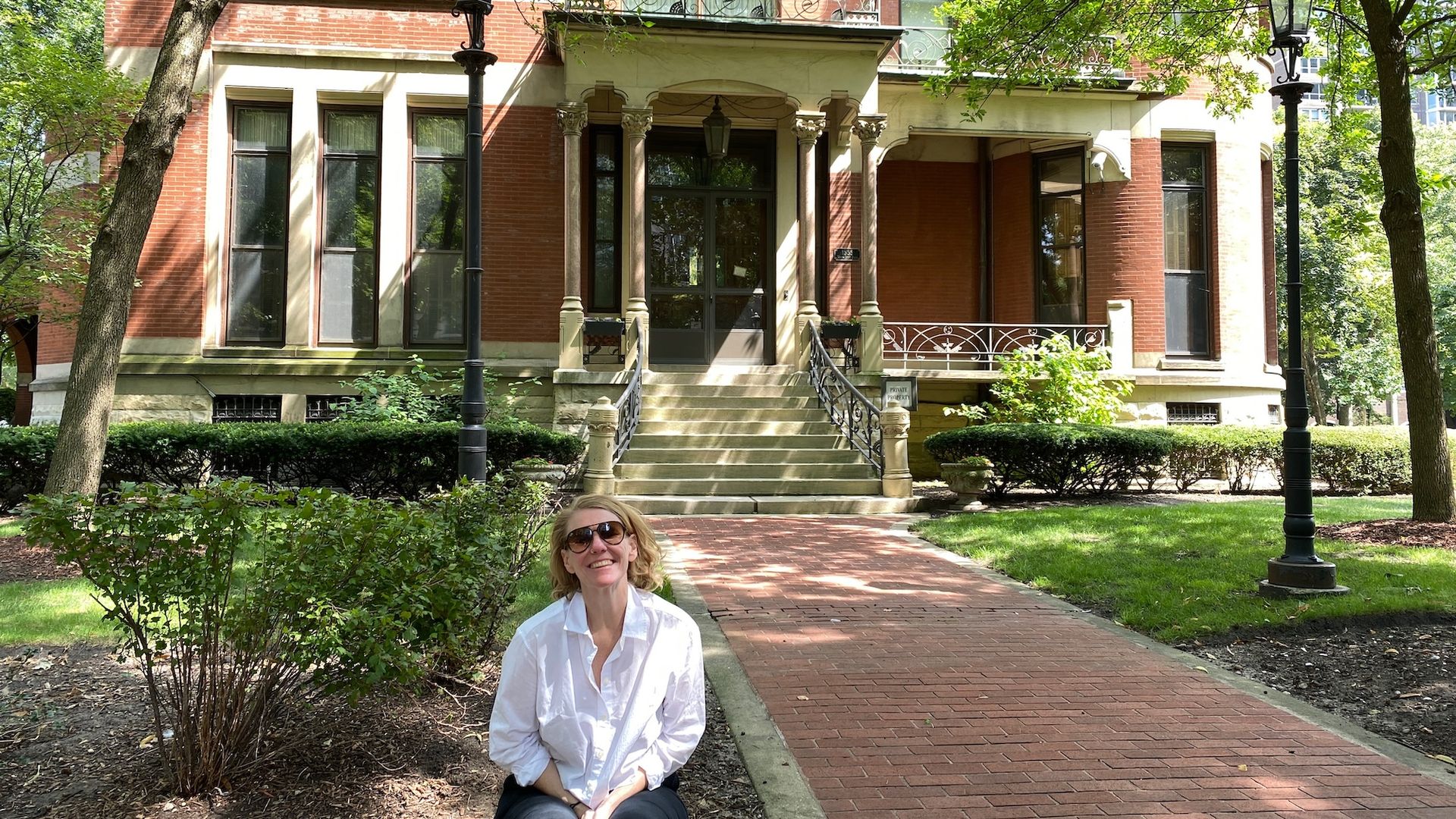 Woman in white shirt sitting in front of red Queen Anne style mansion