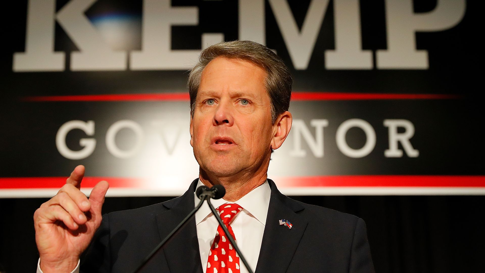 Brian Kemp speaks with a "kemp for governor" sign in the background.