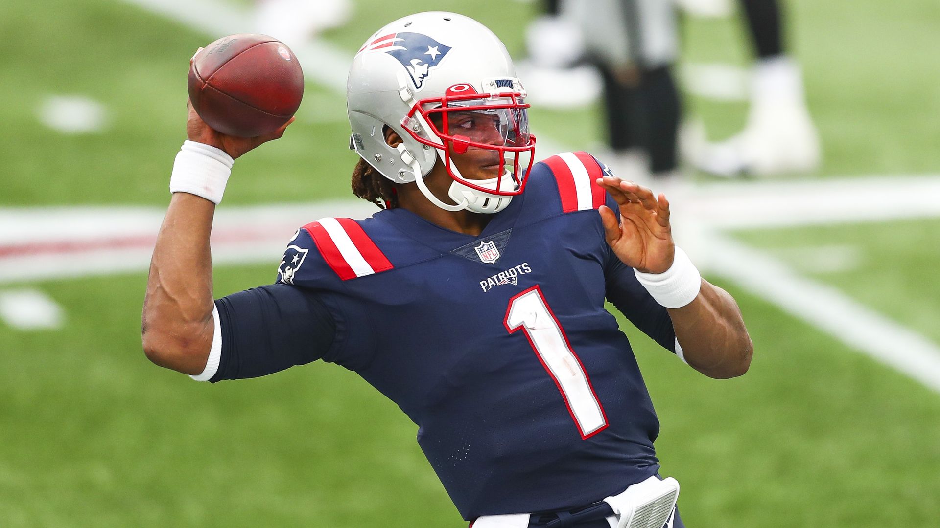 Cam Newton holds a football while wearing a helmet 