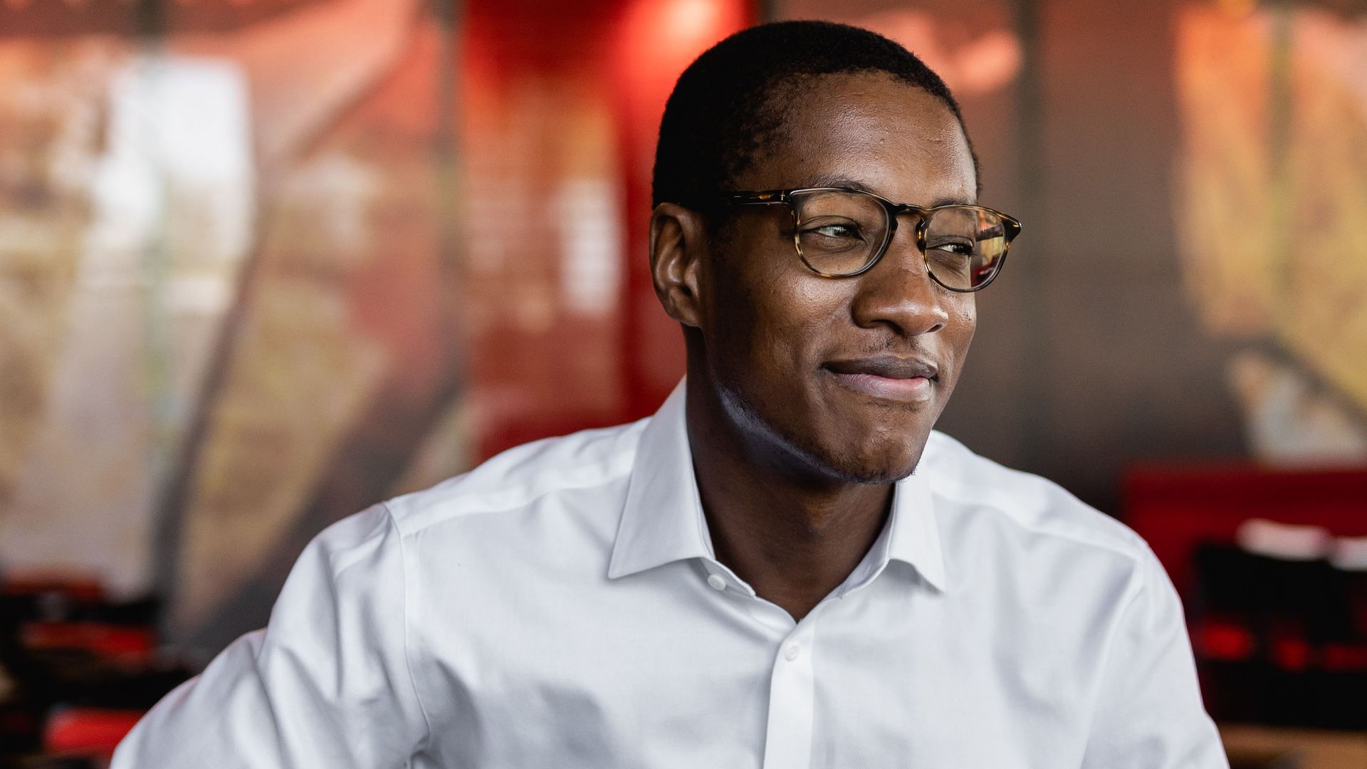 A man with a white shirt smiles and looks to the side.