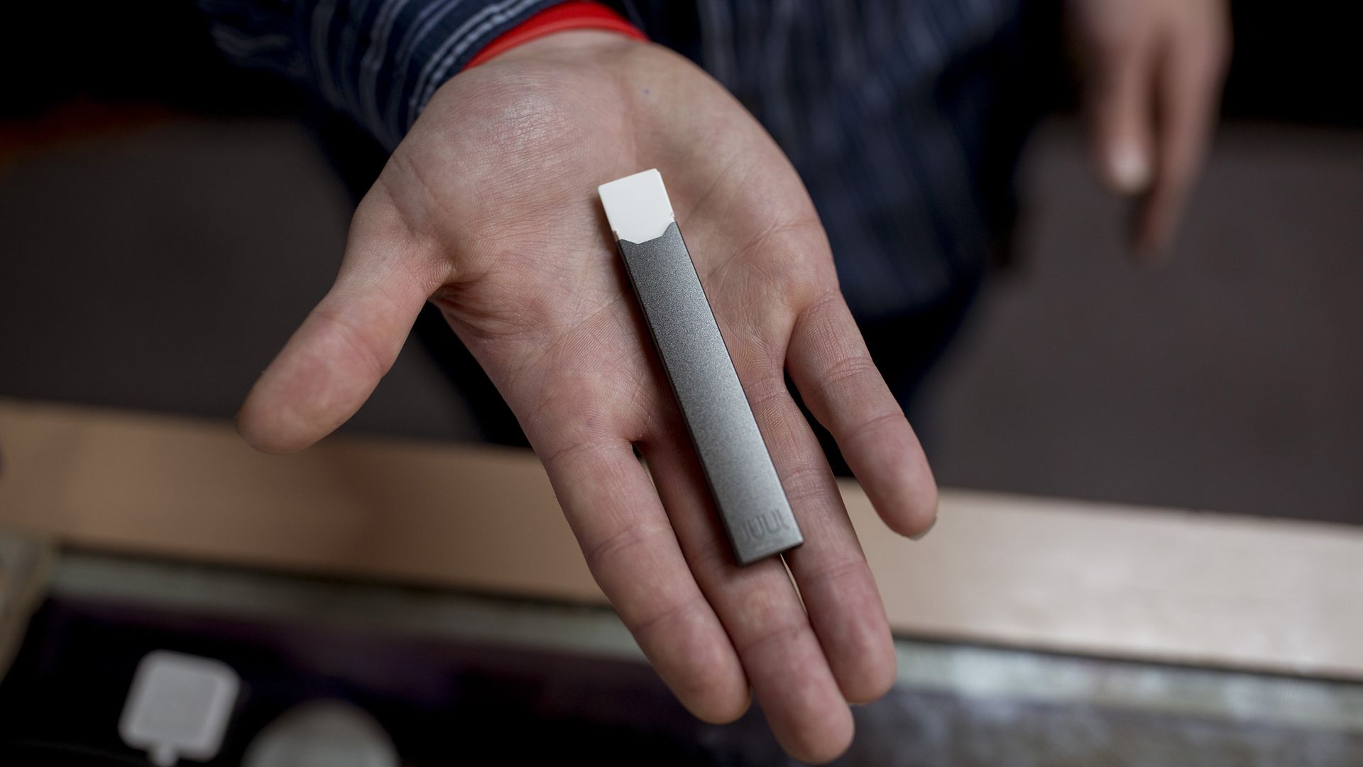 In this image, someone holds a small, rectangular Juul vape in the palm of their outstretched hand, facing the camera.