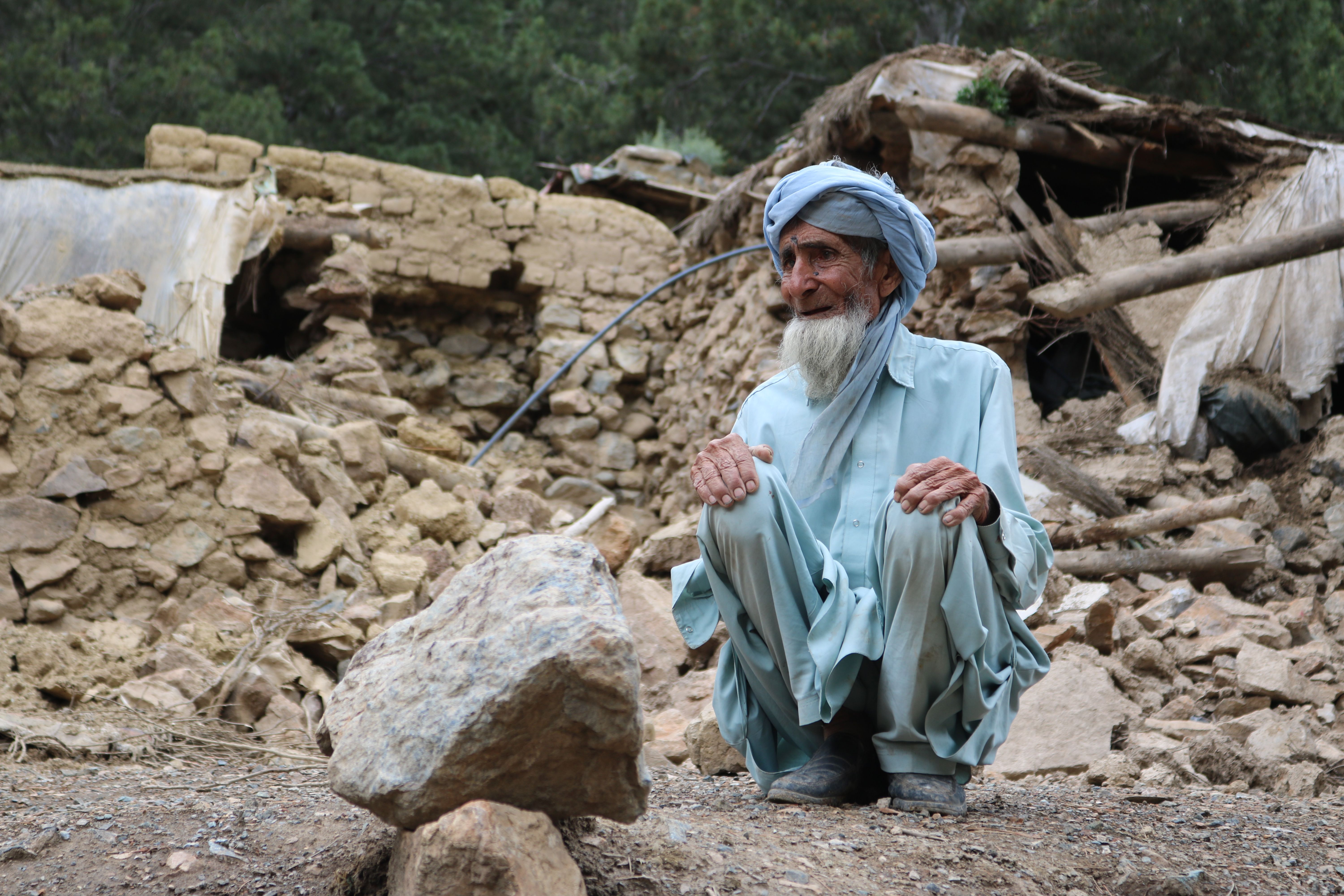 An older man sitting in rubble looking at the destruction of an earthquake. 