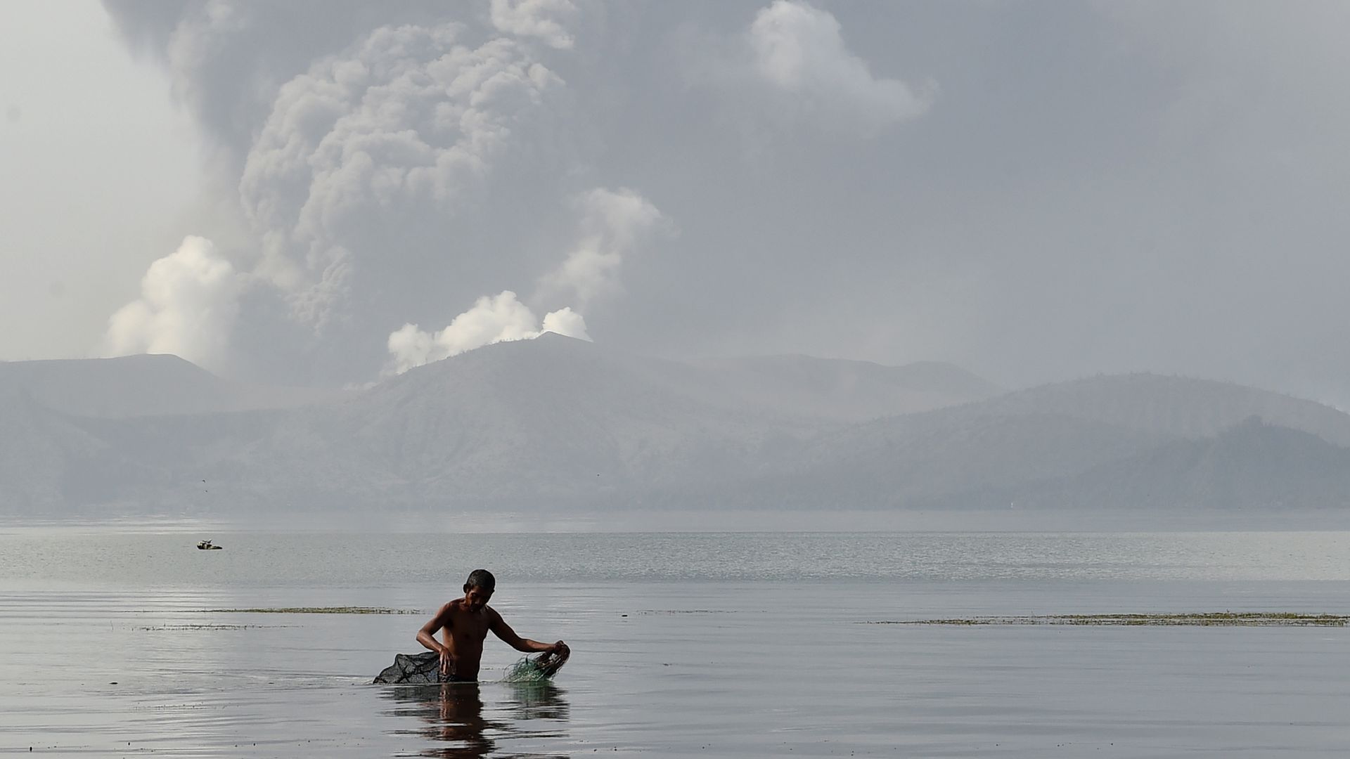 A fisherman wades with his nets in the waters of Taal Lake as the Taal volcano spews ash as seen from Tanauan town in Batangas province, south of Manila, on Monday. 