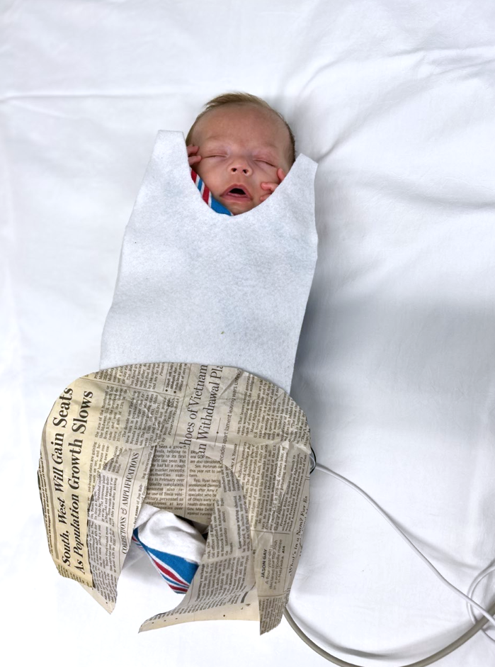 Photo shows a baby with a newspaper dress.