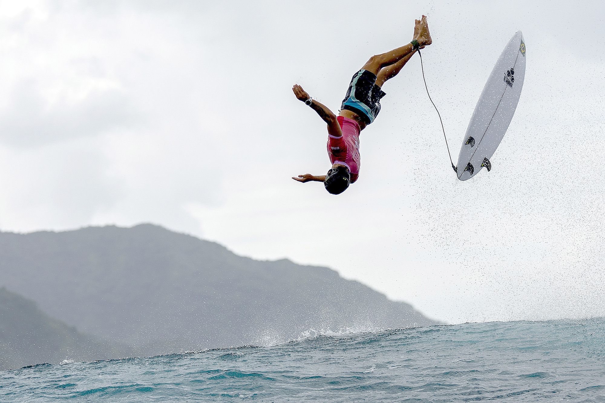 A surfer flips over a wave with his board flying in the air.