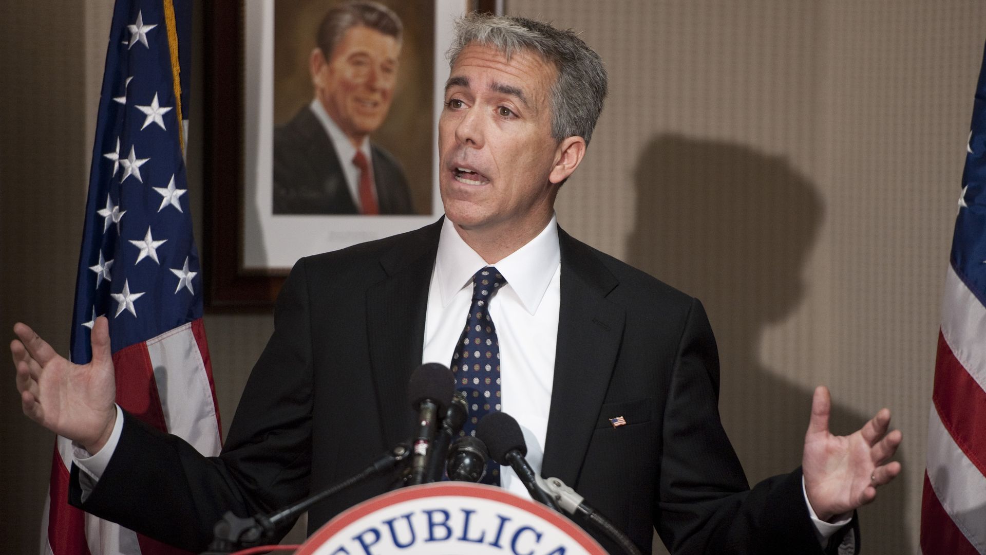In this image, Walsh speaks at a podium stationed between two American flags. A sign that says "National Republican Committee" is on the front of the podium, mostly out of frame.