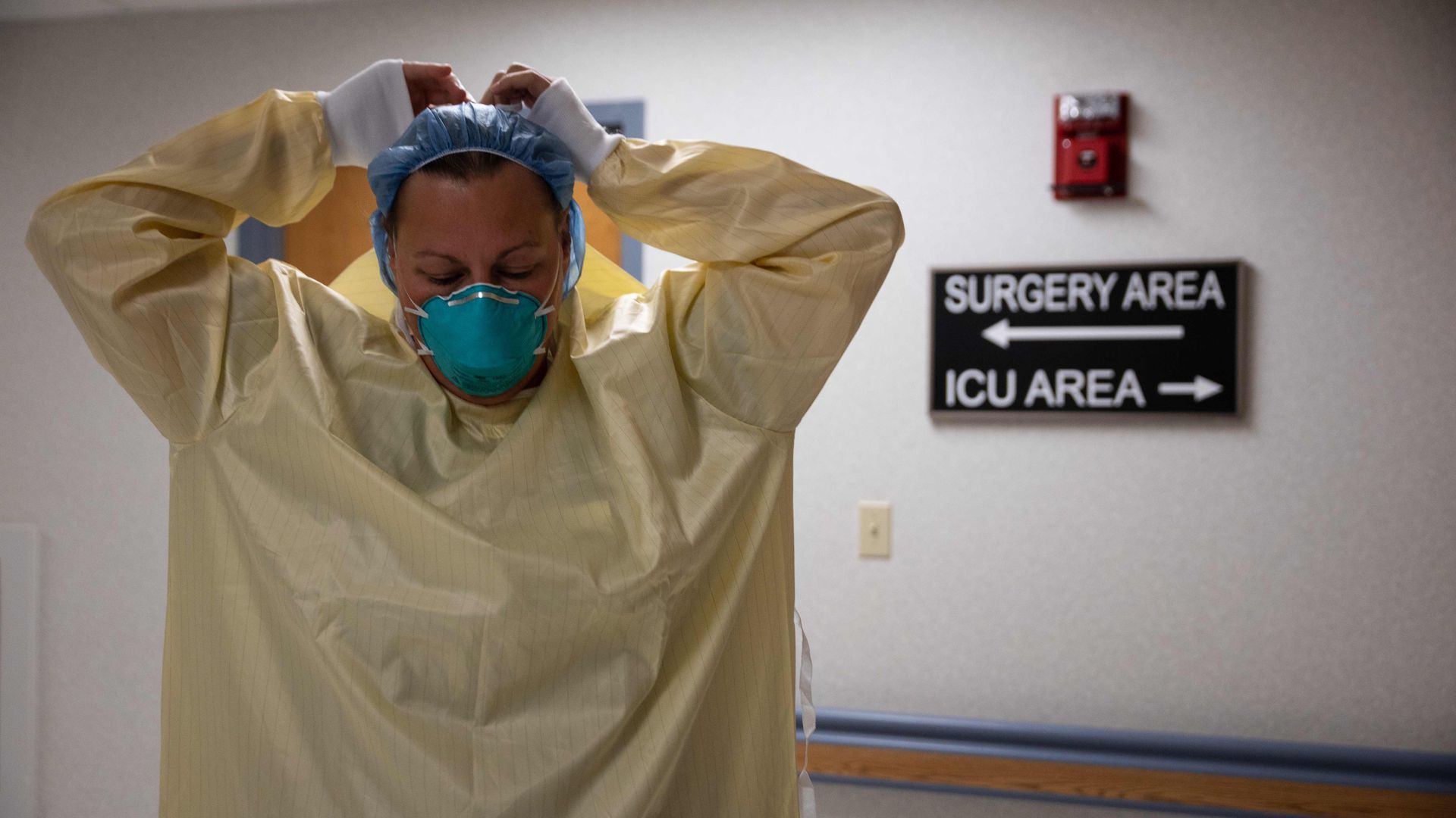 A picture of a health care professional wearing a yellow isolation suit putting on a blue N95 mask