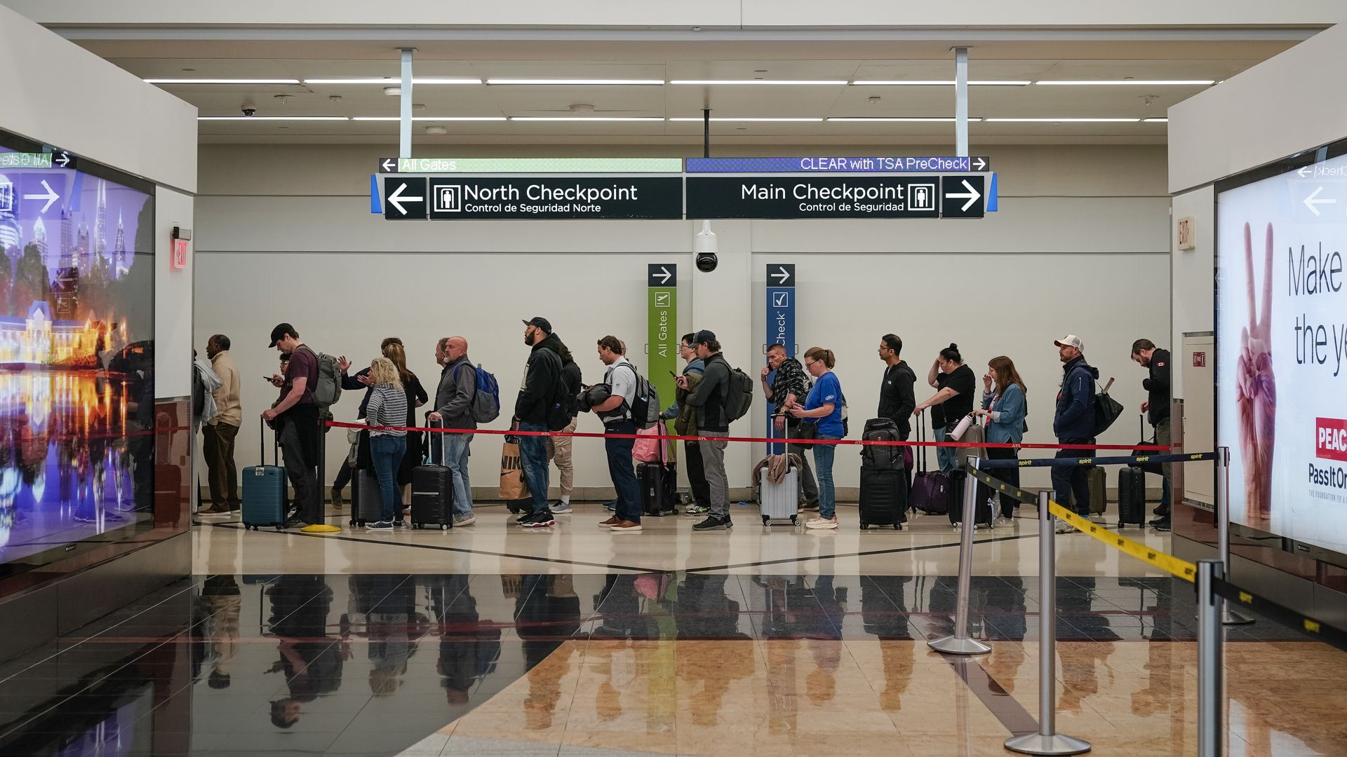 A crowded TSA checkpoint line winds through an airport terminal as travelers wait with luggage.