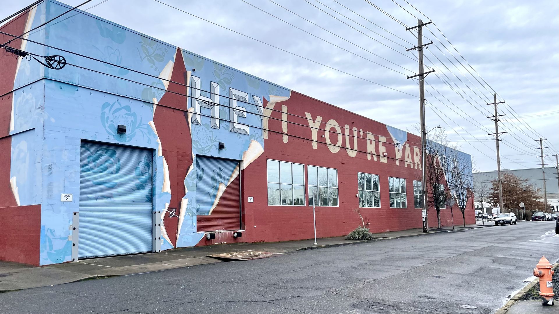 A photo of a blue mural with the words "Hey ! You're part of it" on the side of a brick-colored building.