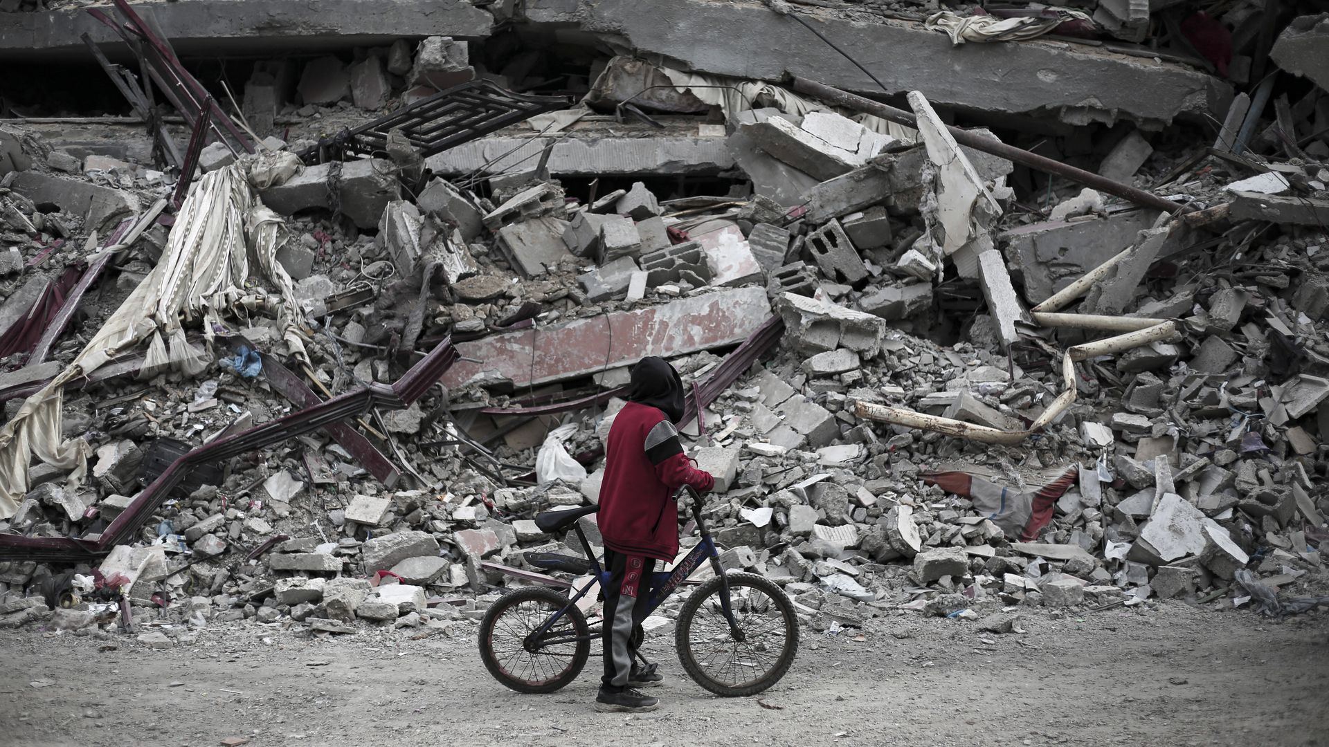 A Palestinian boy along with his bicycle looks at the rubble of a house destroyed by Israeli bombardment in Rafah