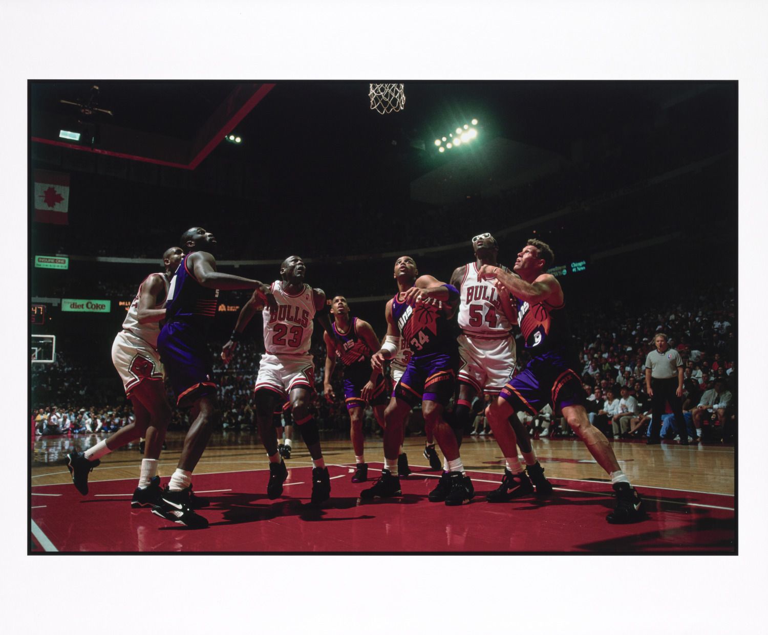 Basketball players from Chicago Bulls in white and Phoenix Suns in purple battling for position under the hoop during a game with a crowd watching in the background.