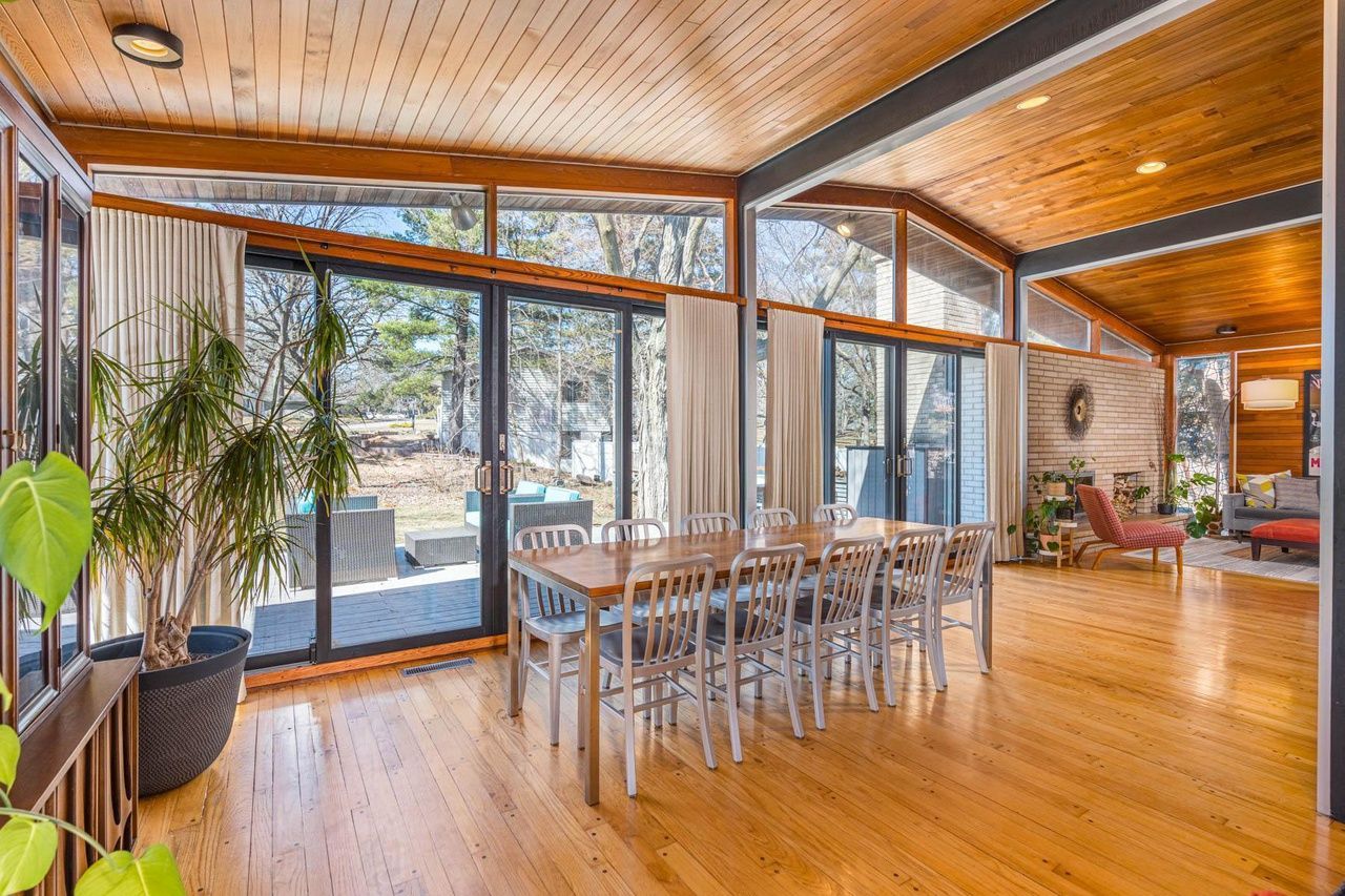 A mid-century modern style home with wooden ceilings, glass walls and a large table and chairs.