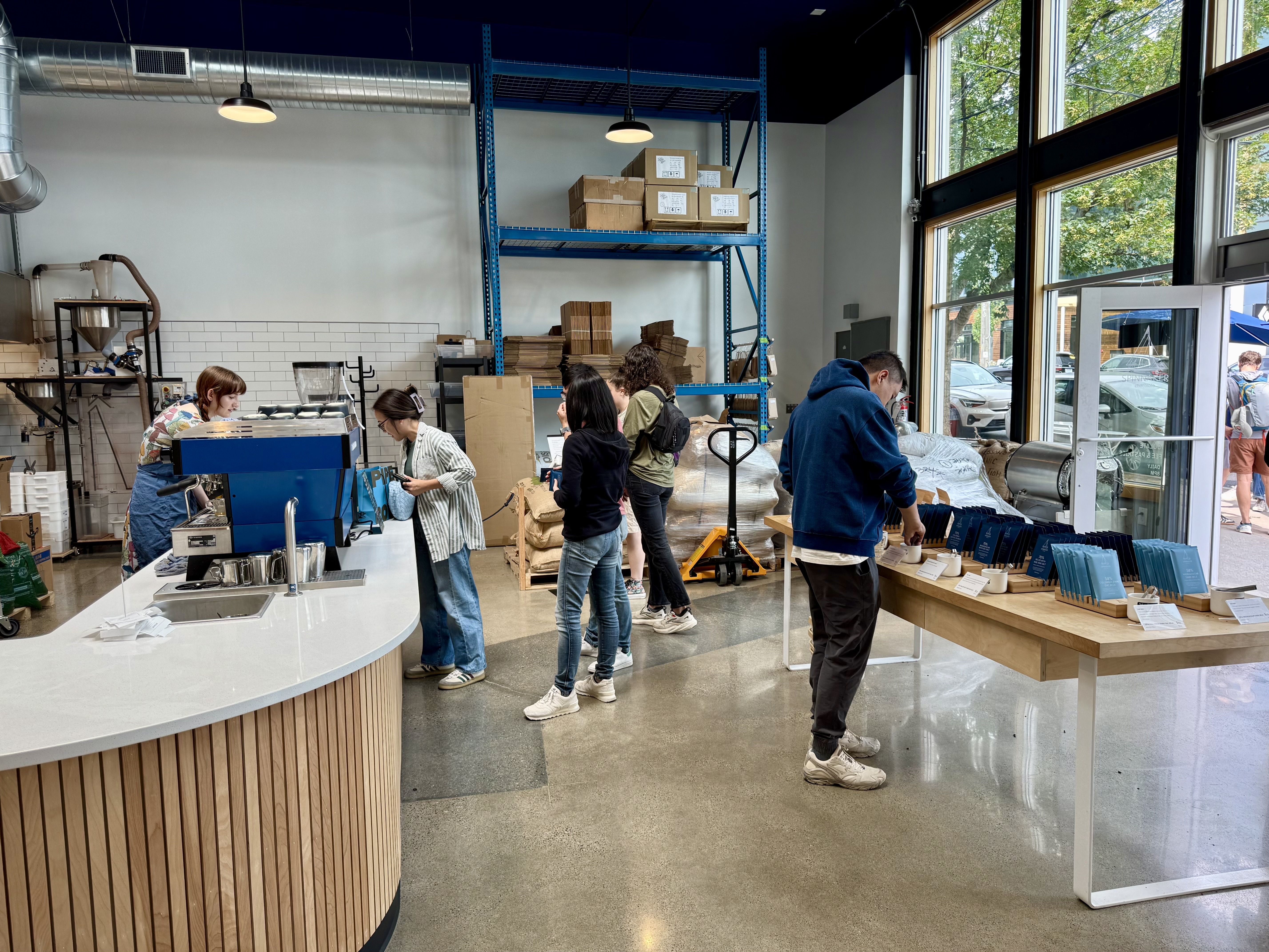 People browse a selection of chocolate bars inside Spinnaker Chocolate's new cafe and factory in Fremont, with others ordering a coffee at the modern bar counter.