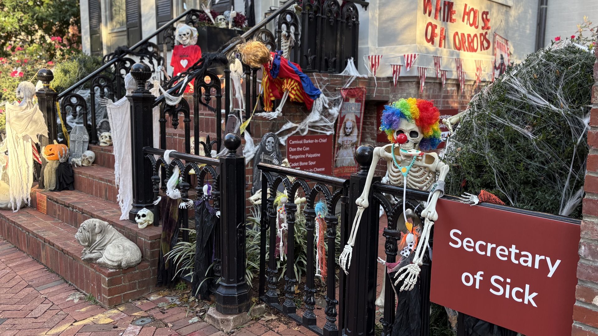 Porch decorated for Halloween with skeletons, skulls, cobwebs, and signs including "Secretary of Sick" and "White House of Horrors" in daylight.