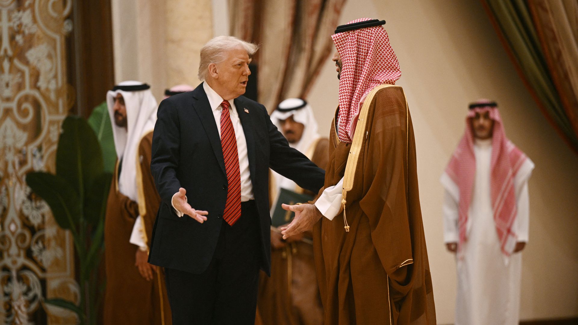 Two men, one in a suit and one in formal Arab dress, stand next to each other.