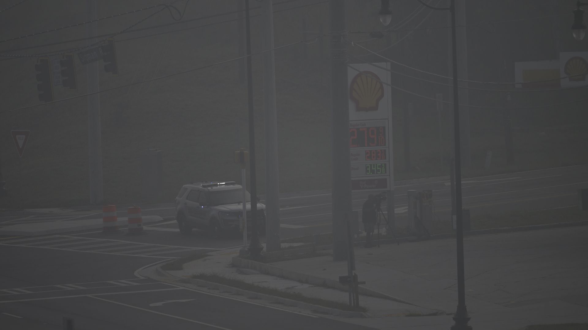 An SUV with sirens blocks an intersection in front of a gas station in a severely hazy environment