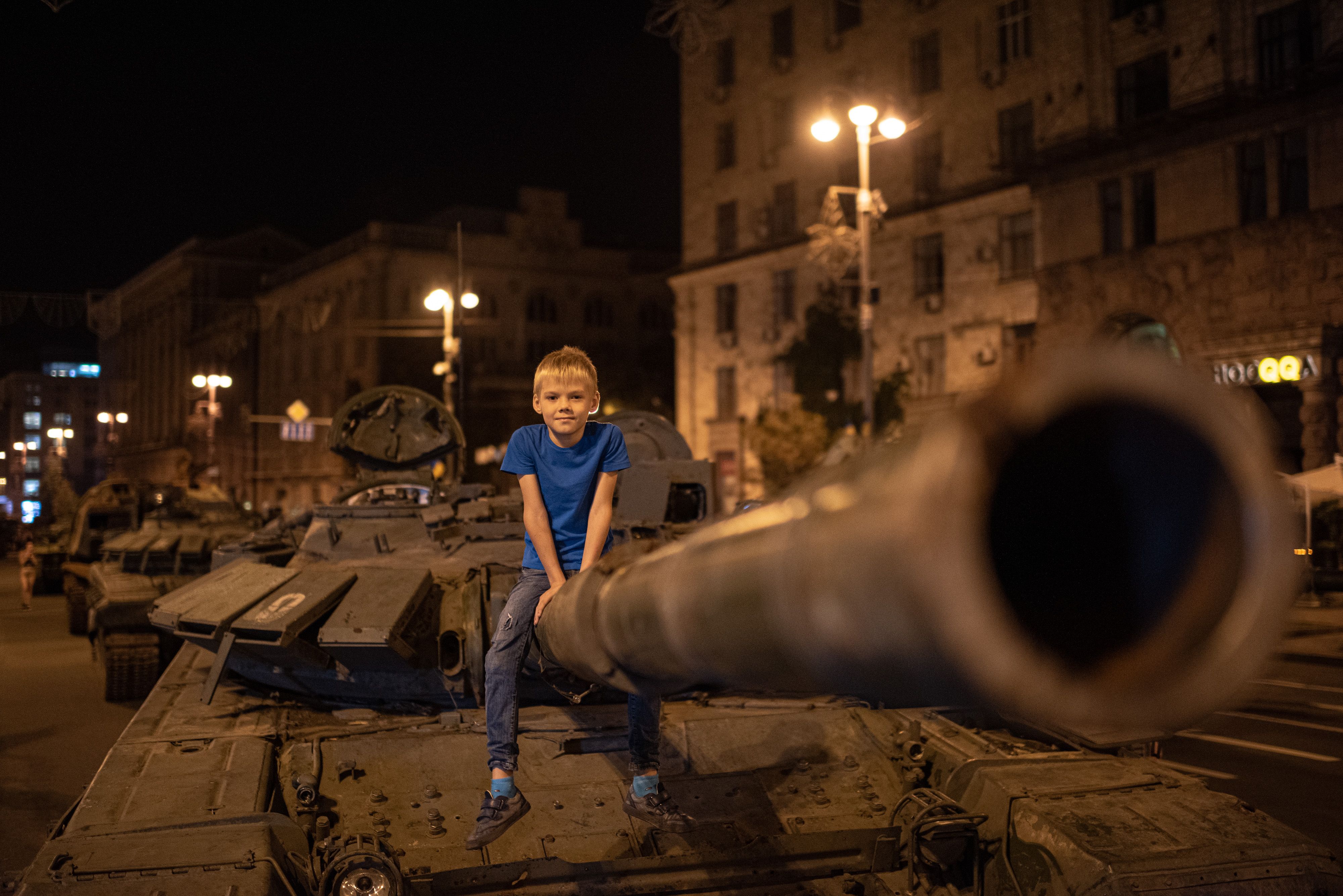 A boy poses for a photograph on top of a burnt-out Russian tank 