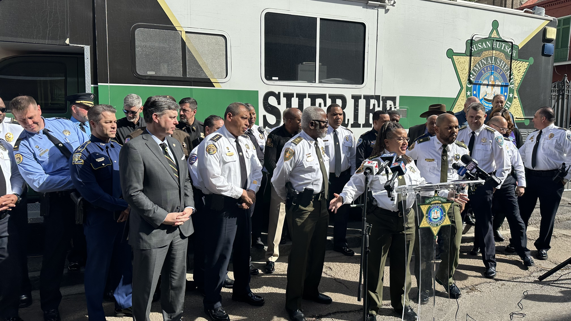 Orleans Parish Sheiff Susan Hutson speaks at a podium. She is flanked by over a dozen other regional law enforcement officers.