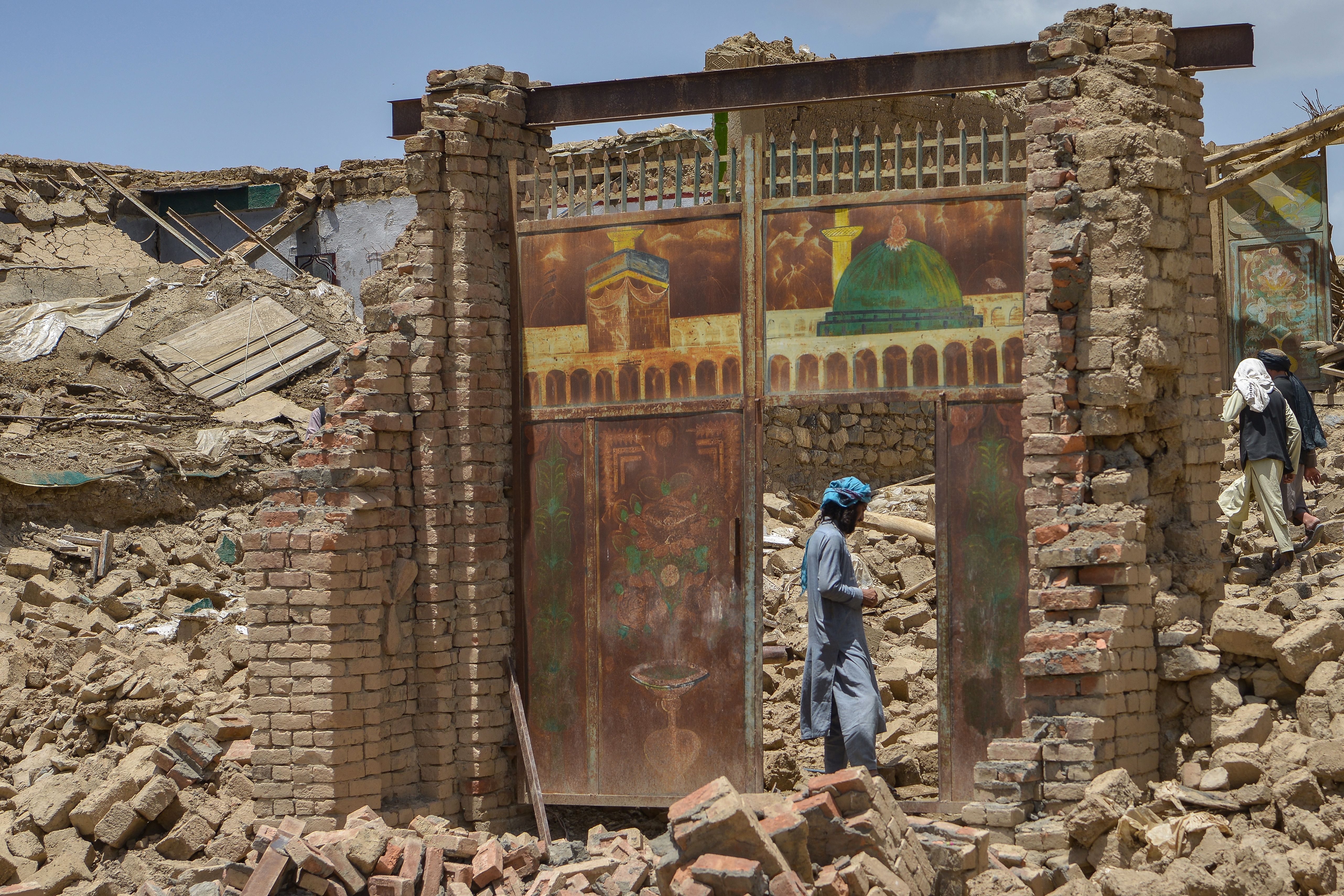 A man seen through a destroyed door frame with images of Islamic buildings painted on the frame.