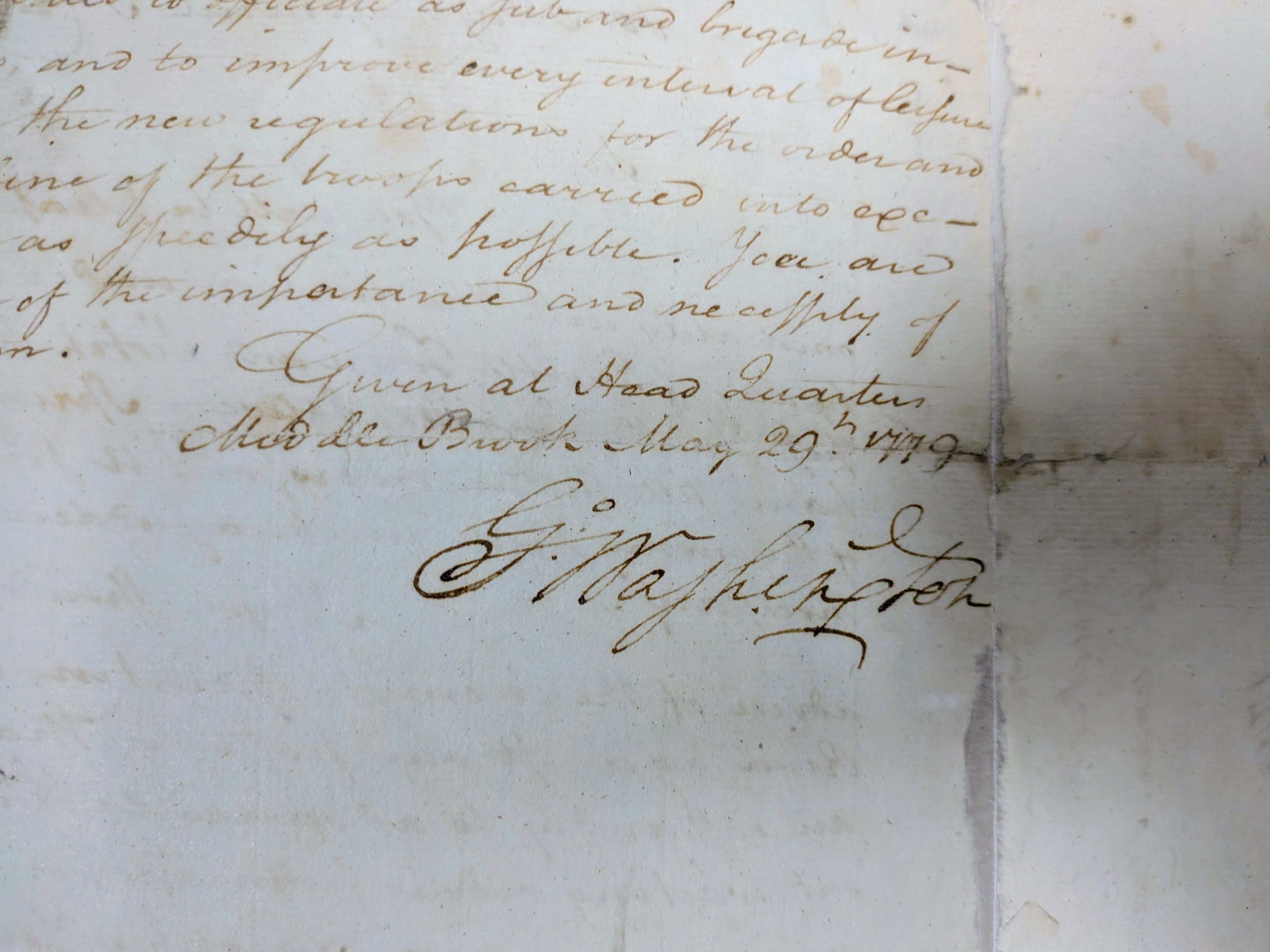 Close-up of an aged document with brown cursive handwriting on light paper. Script is ornate, with a visible vertical seam along the right; the decorative signature of George Washington appears toward the bottom.