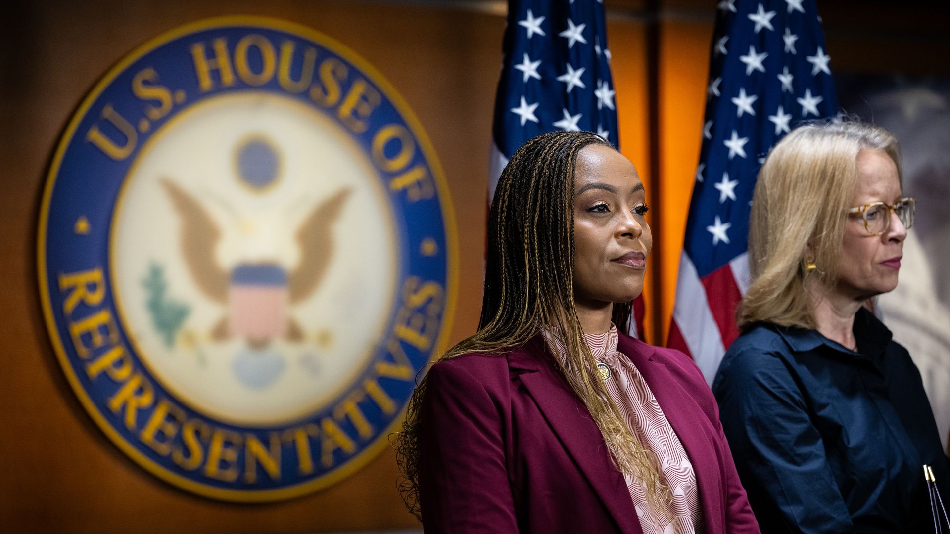 Black woman in maroon blazer stands before sign reading "US House of Representatives" 