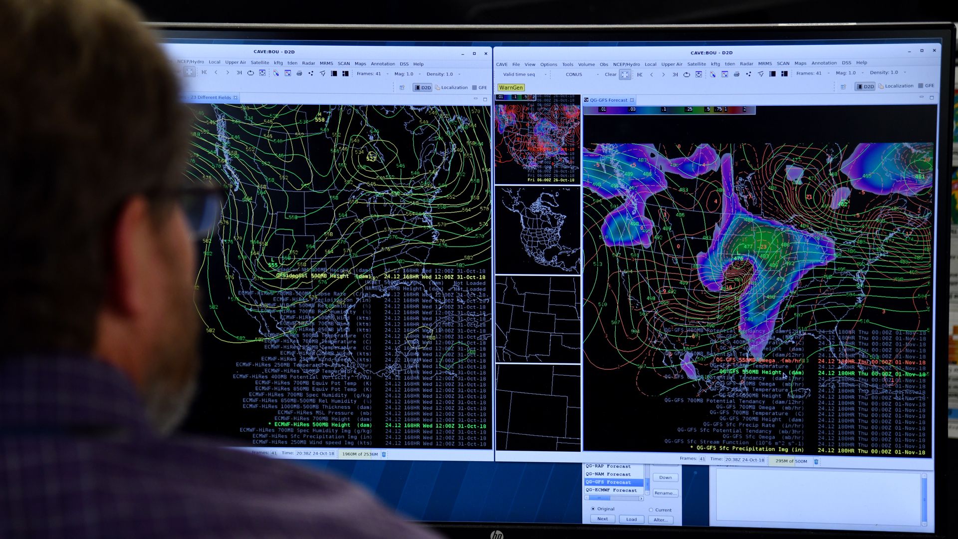 In this image, a man with glasses looks at two computer monitors with wind patterns displayed.