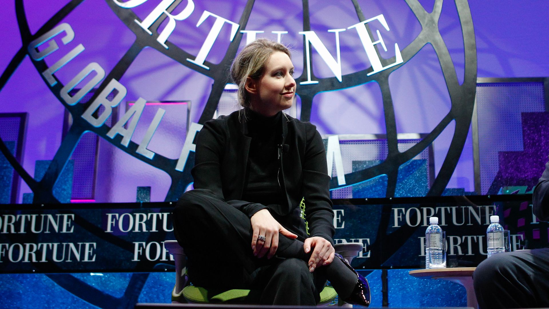 Holmes sits on a stage in a black turtleneck