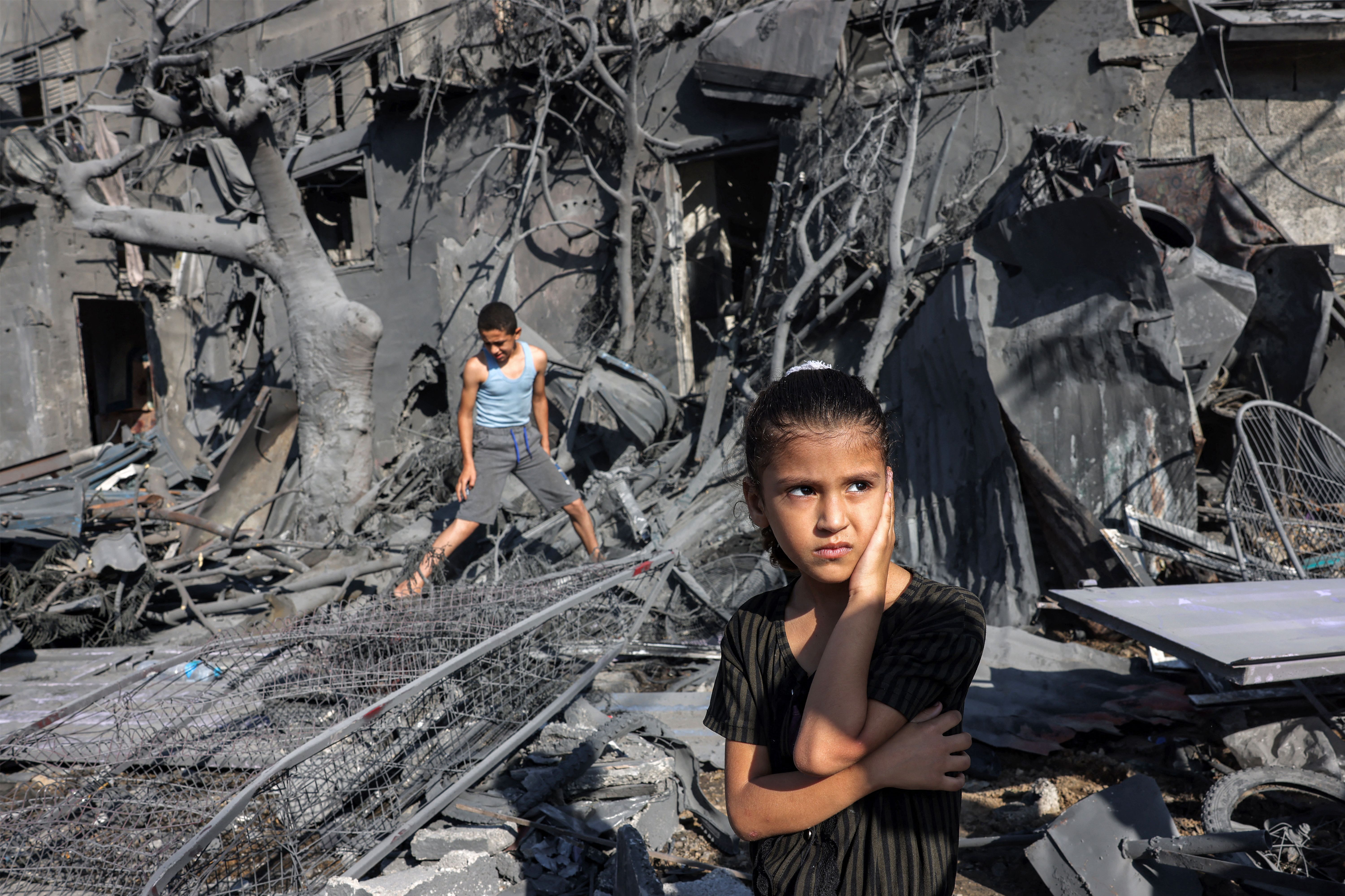 Two children stand in the rubble of a building. 