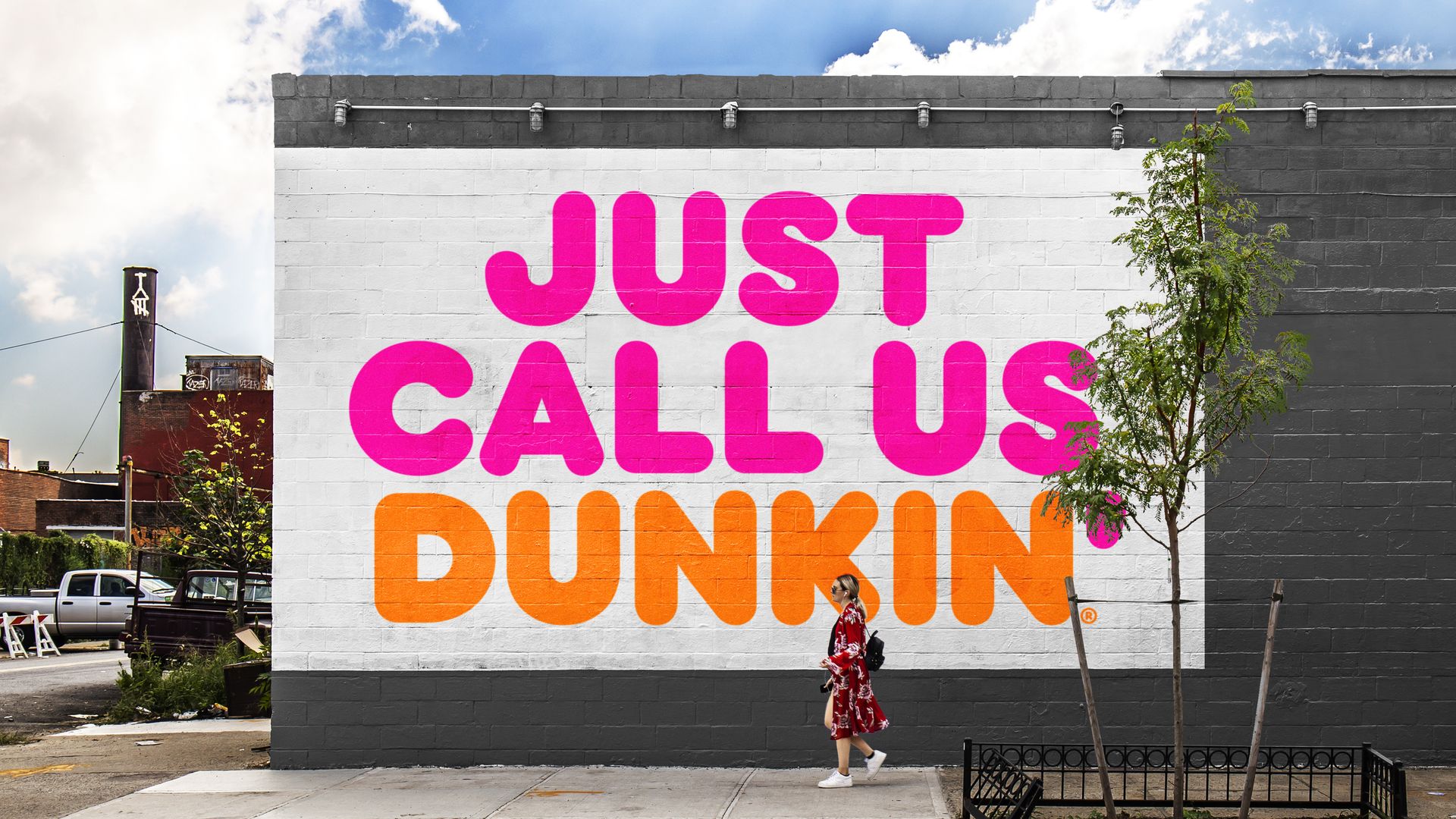A woman walks by a building with a large sign on the outside that says JUST CALL US DUNKIN'