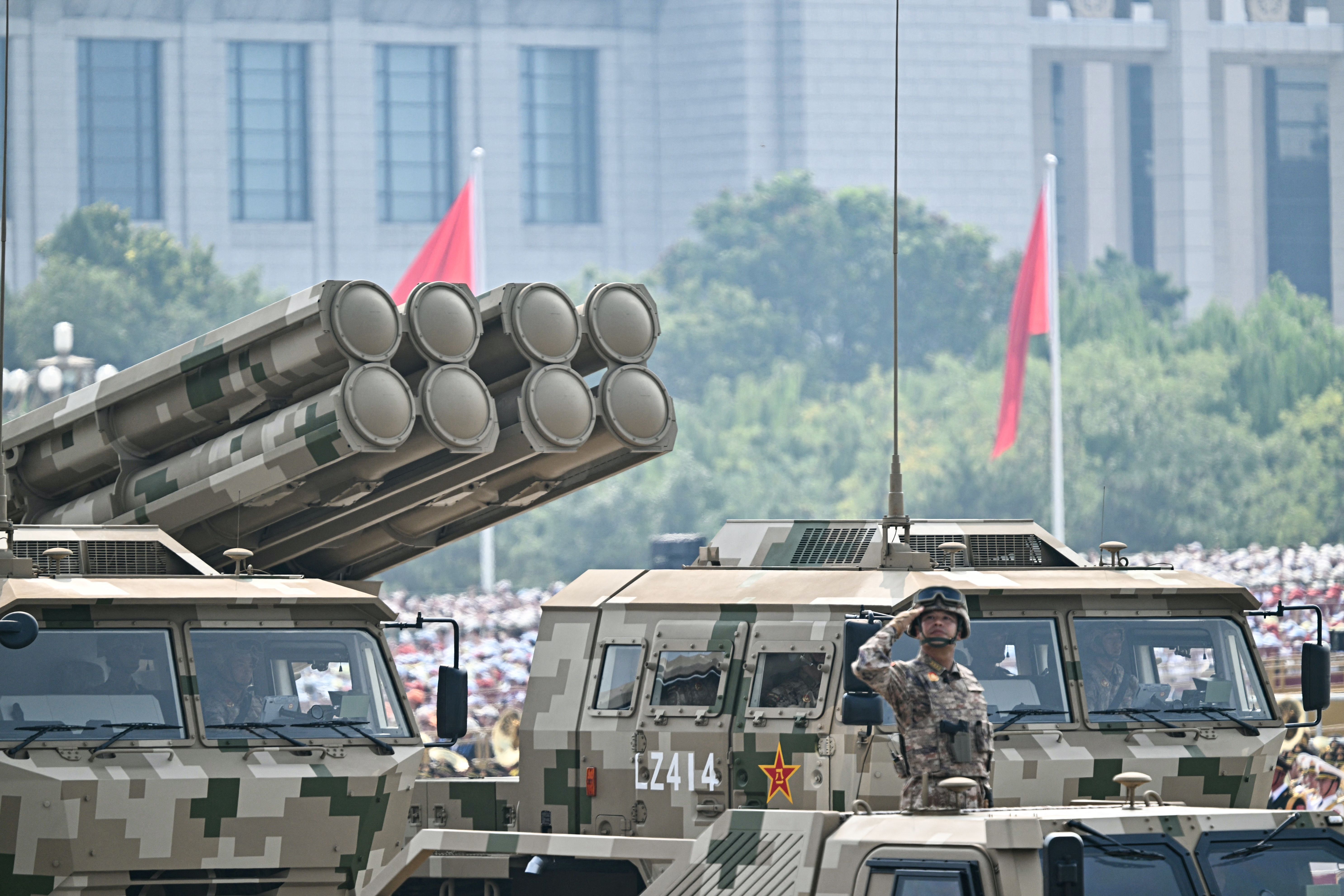 A Chinese officer aboard a tank dressed in khaki salutes during a military parade.
