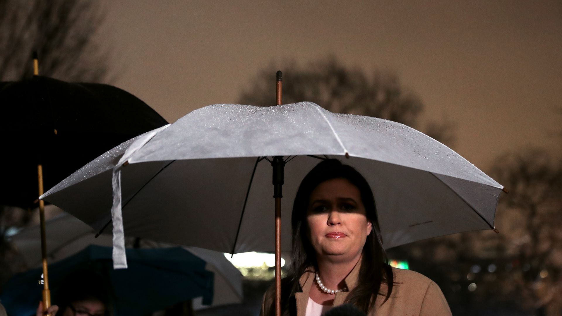 Sarah Sanders holding an umbrella over her head so that it shades part of her eyes
