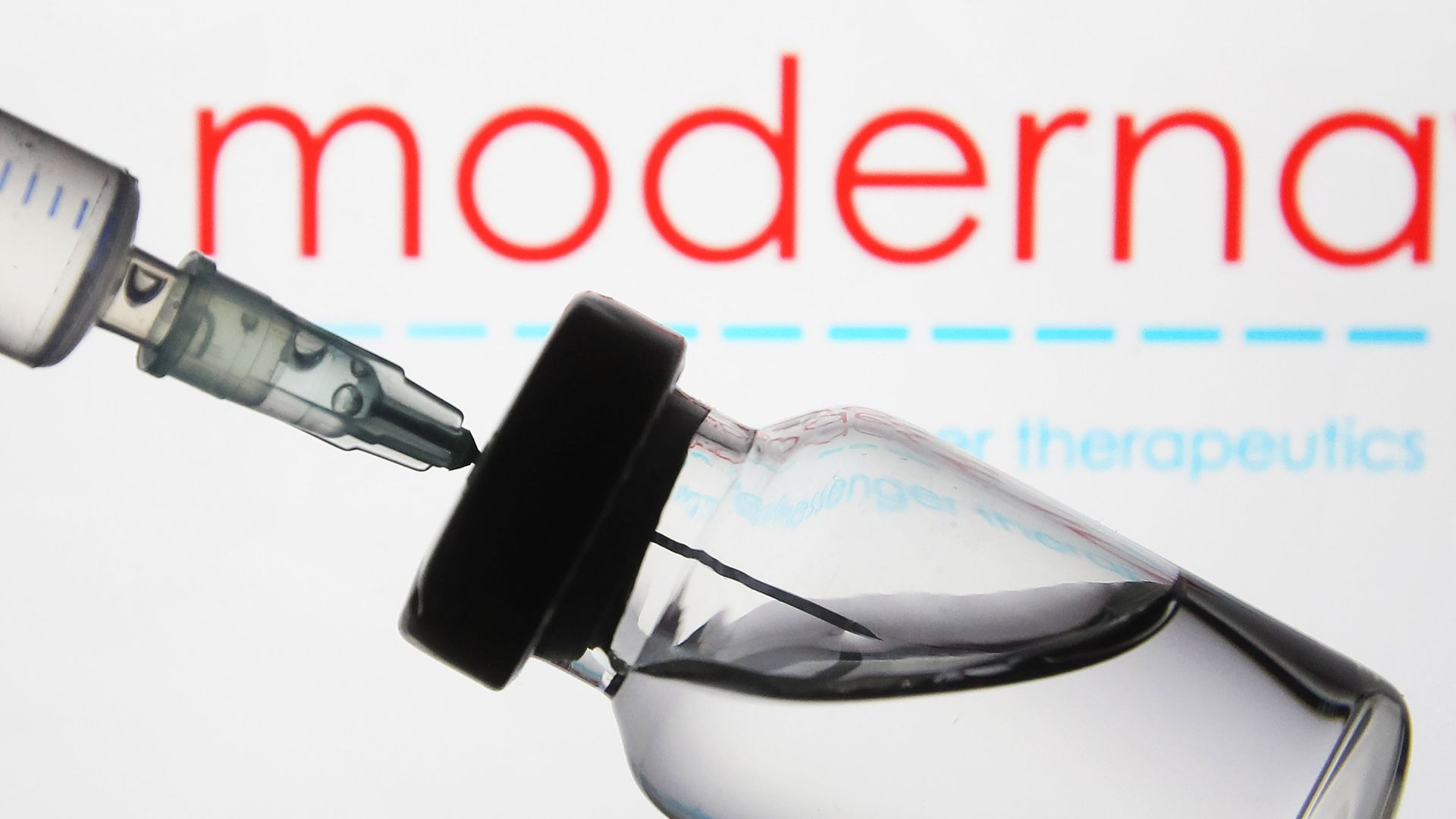 A medical syringe and a vial in front of the Moderna logo