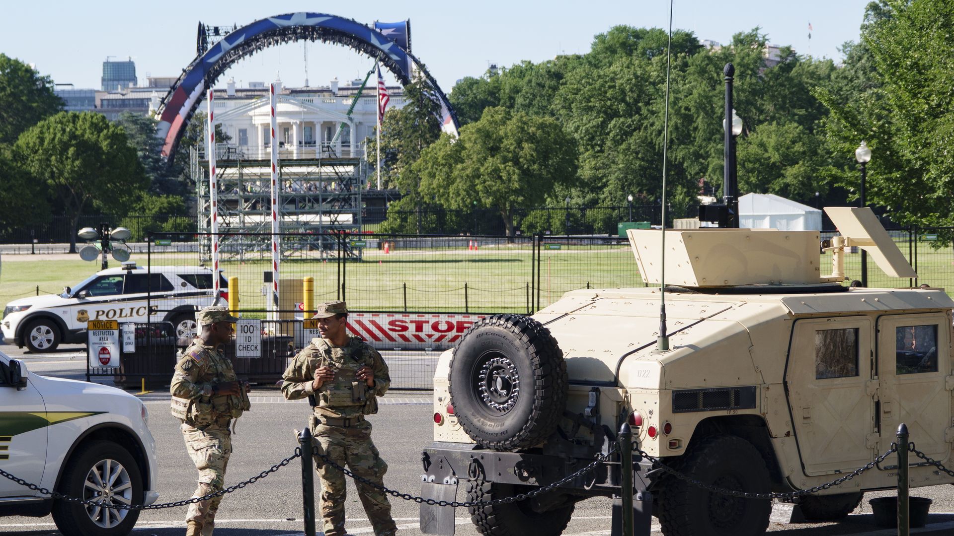 National Guard soldiers stand next to a military vehicle, with the White House and UFC fighting cage stage on the Ellipse in the background