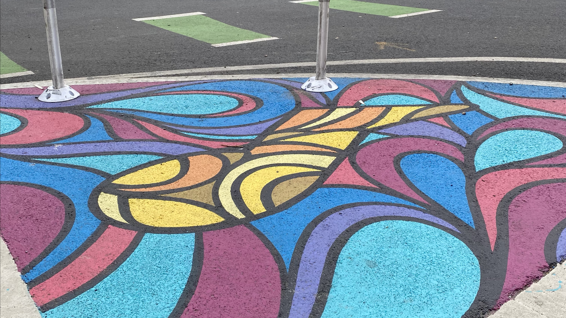 A ground mural of brightly painted, abstract shapes on 8th and V NW in D.C. One white car is in the background.