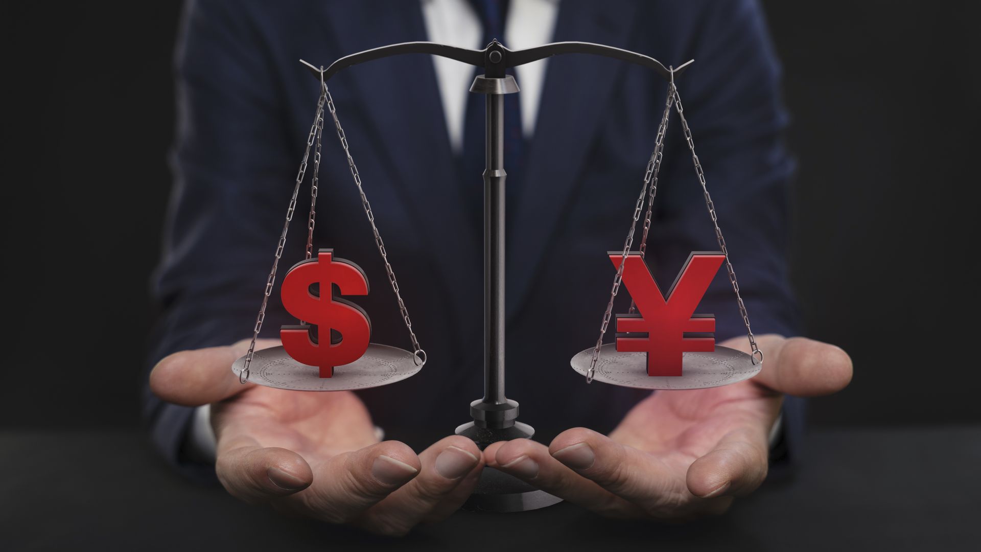 Photo illustration of person holding hands under 2 scale balance of dollar and yuan signs