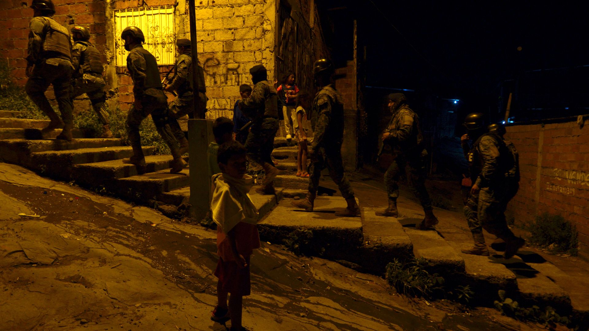 Soldiers walking up some steps while in line patrol in Peru as a child stands on the street