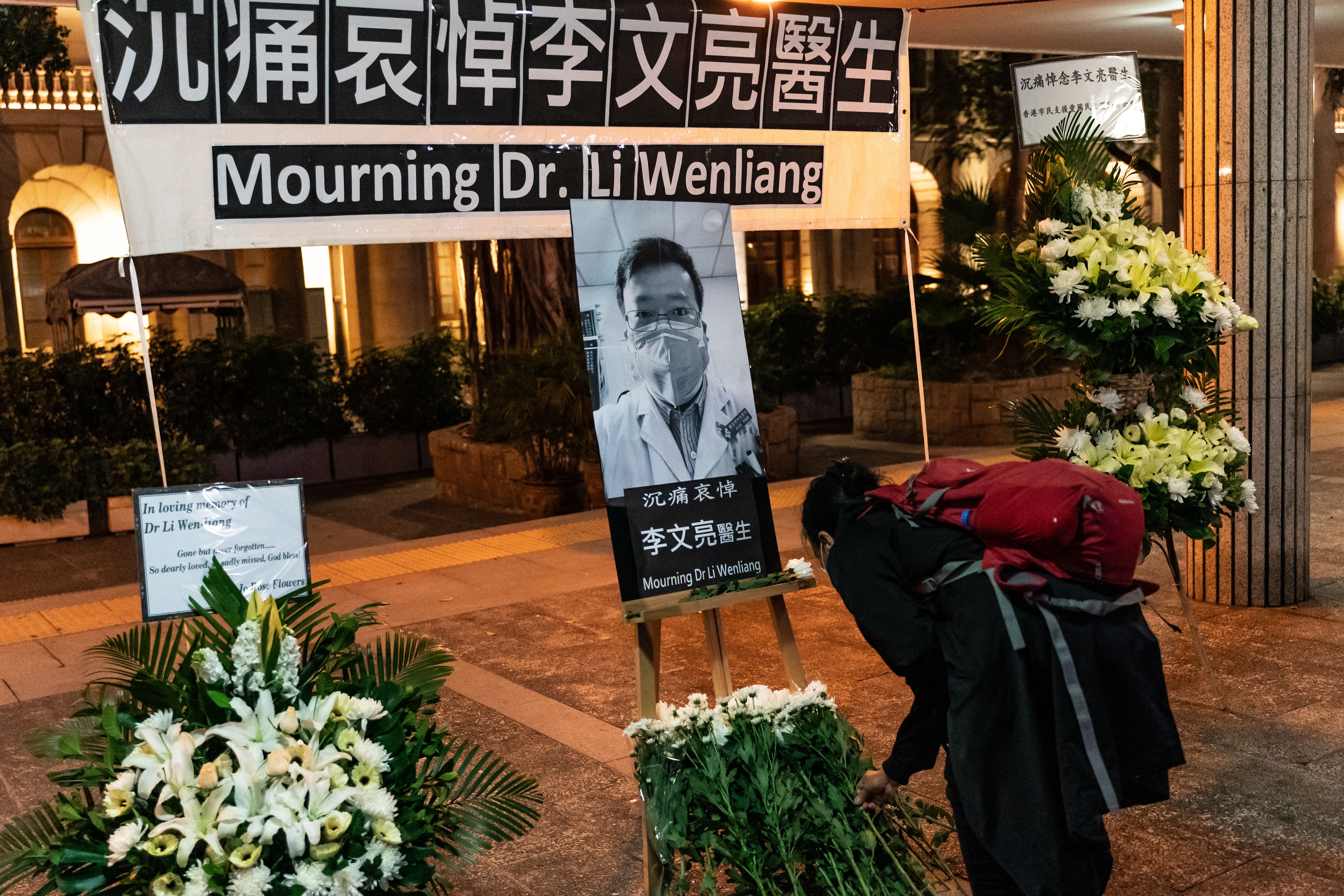 In this image, a sign reads "Mourning Dr. Li Wenliang" and a photo of him stands among flowers